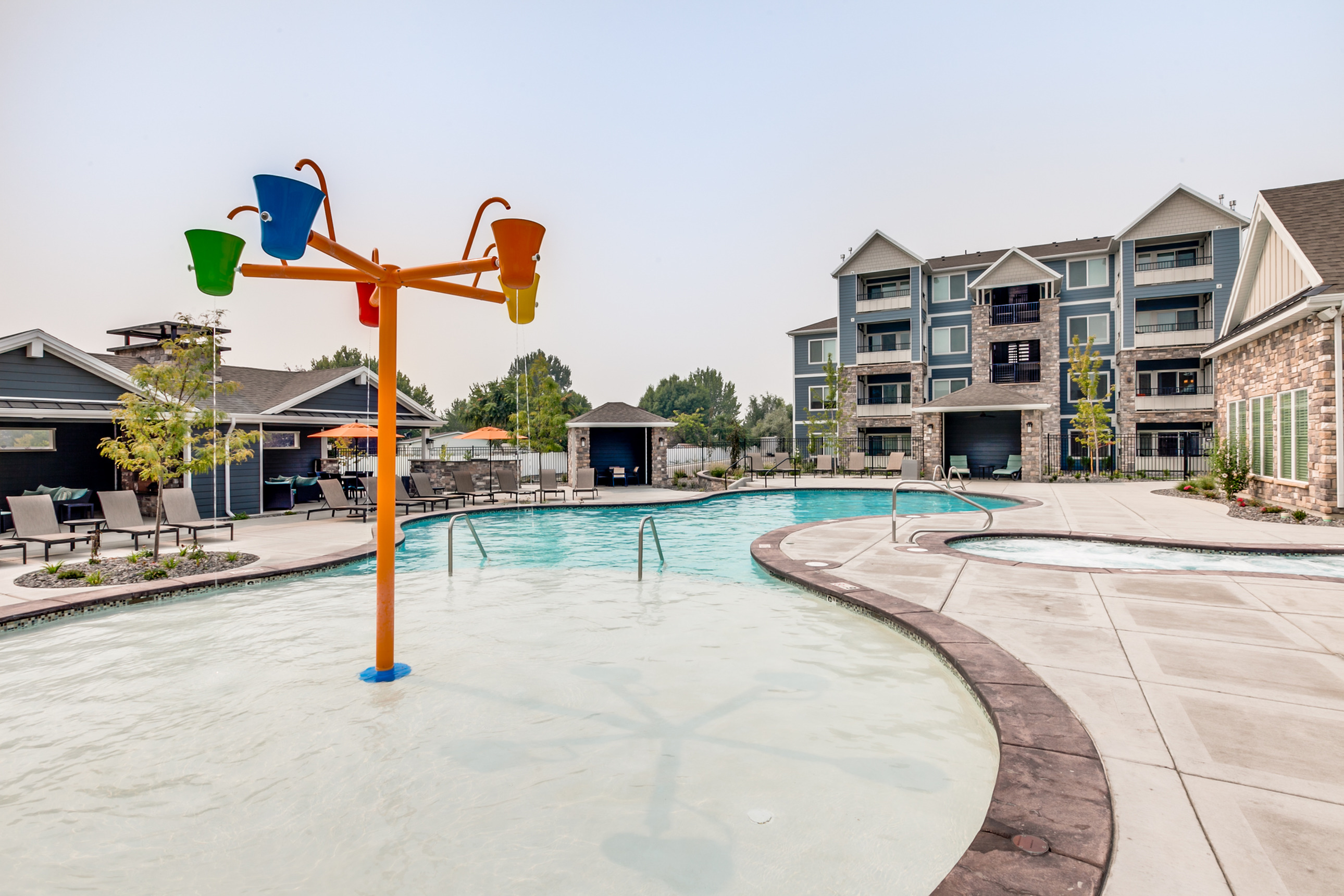 Luxurious apartment complex with a stunning pool area featuring vibrant splash fountains, surrounded by modern seating and lush greenery.