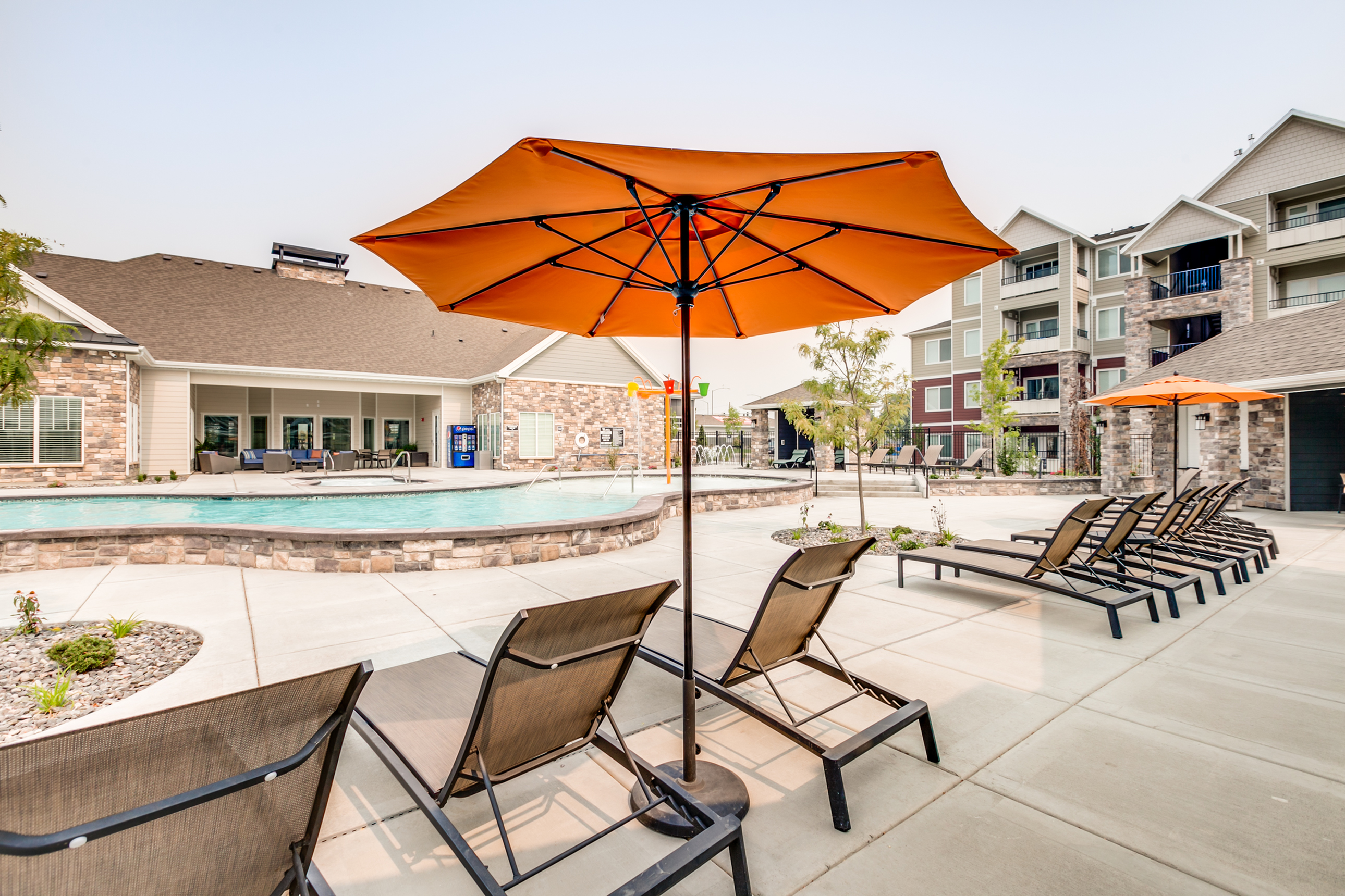 Luxurious apartment complex pool area with stylish loungers and vibrant orange umbrellas, perfect for relaxation and leisure.
