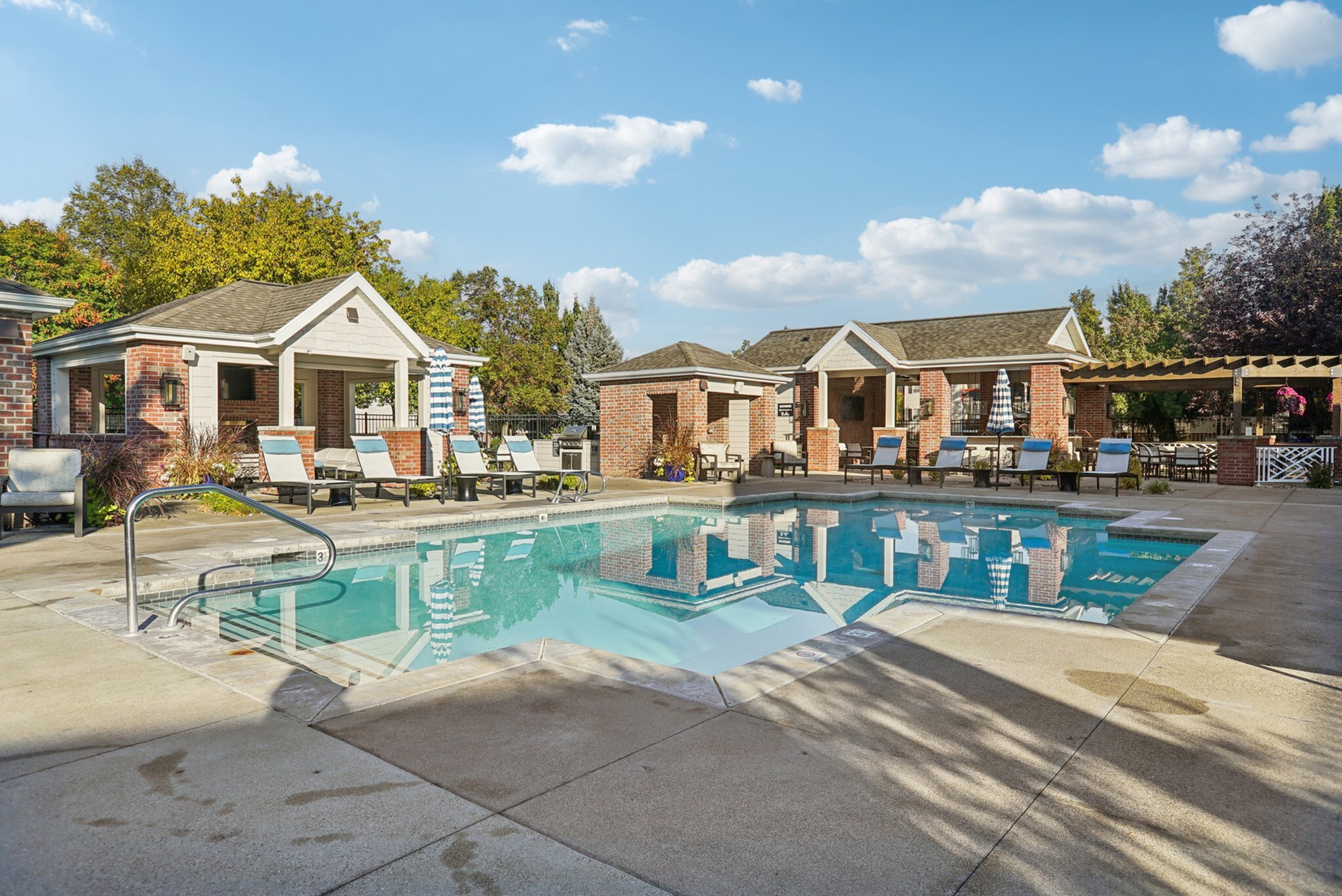 Inviting apartment community showcasing a luxurious outdoor pool with stylish lounge chairs and charming brick cabanas under a clear blue sky.