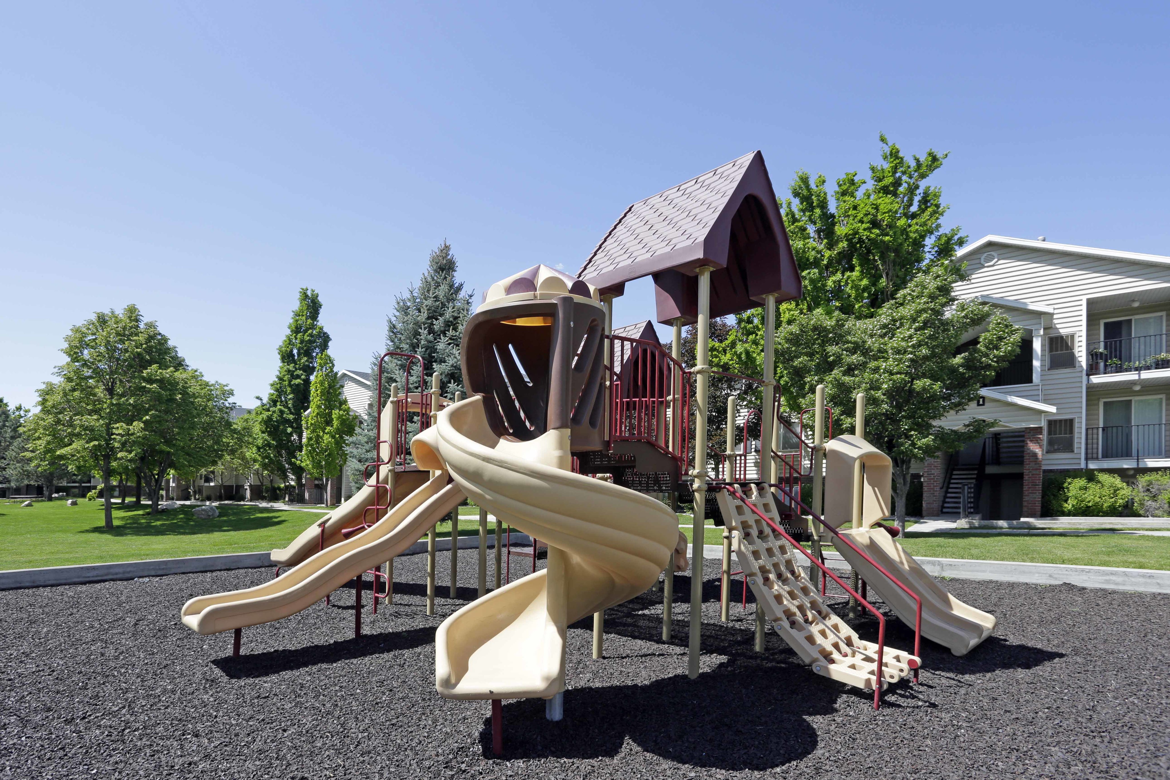 Inviting playground with colorful slides and climbing structures, surrounded by lush green landscape in a vibrant apartment community.