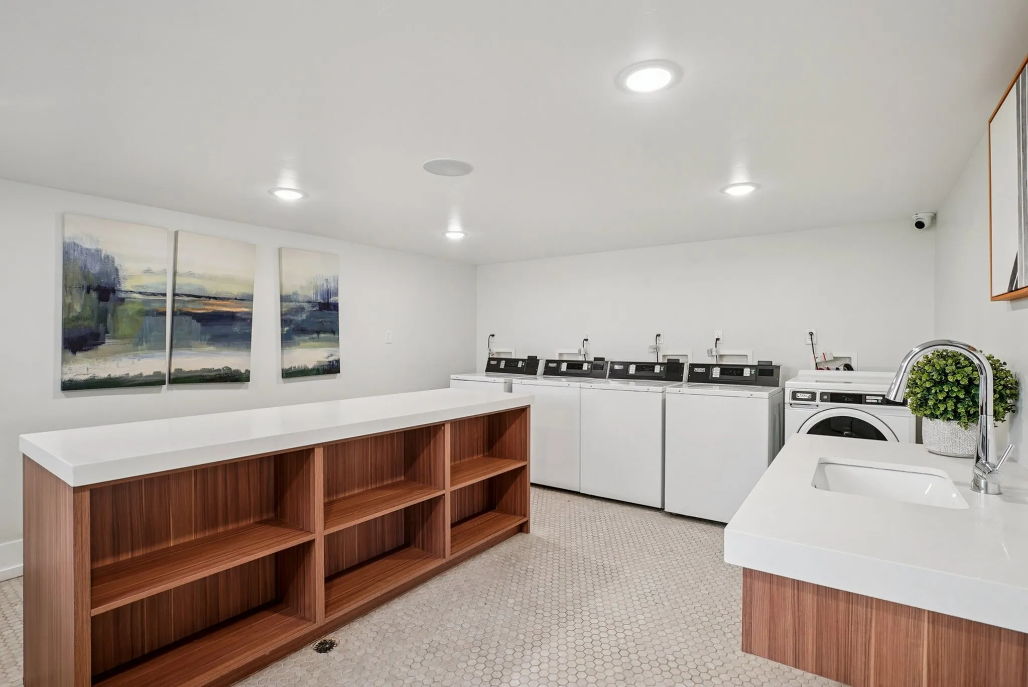 Modern laundry room featuring a sleek countertop, efficient washer and dryer set, and contemporary art. Spacious shelving adds functionality and style.