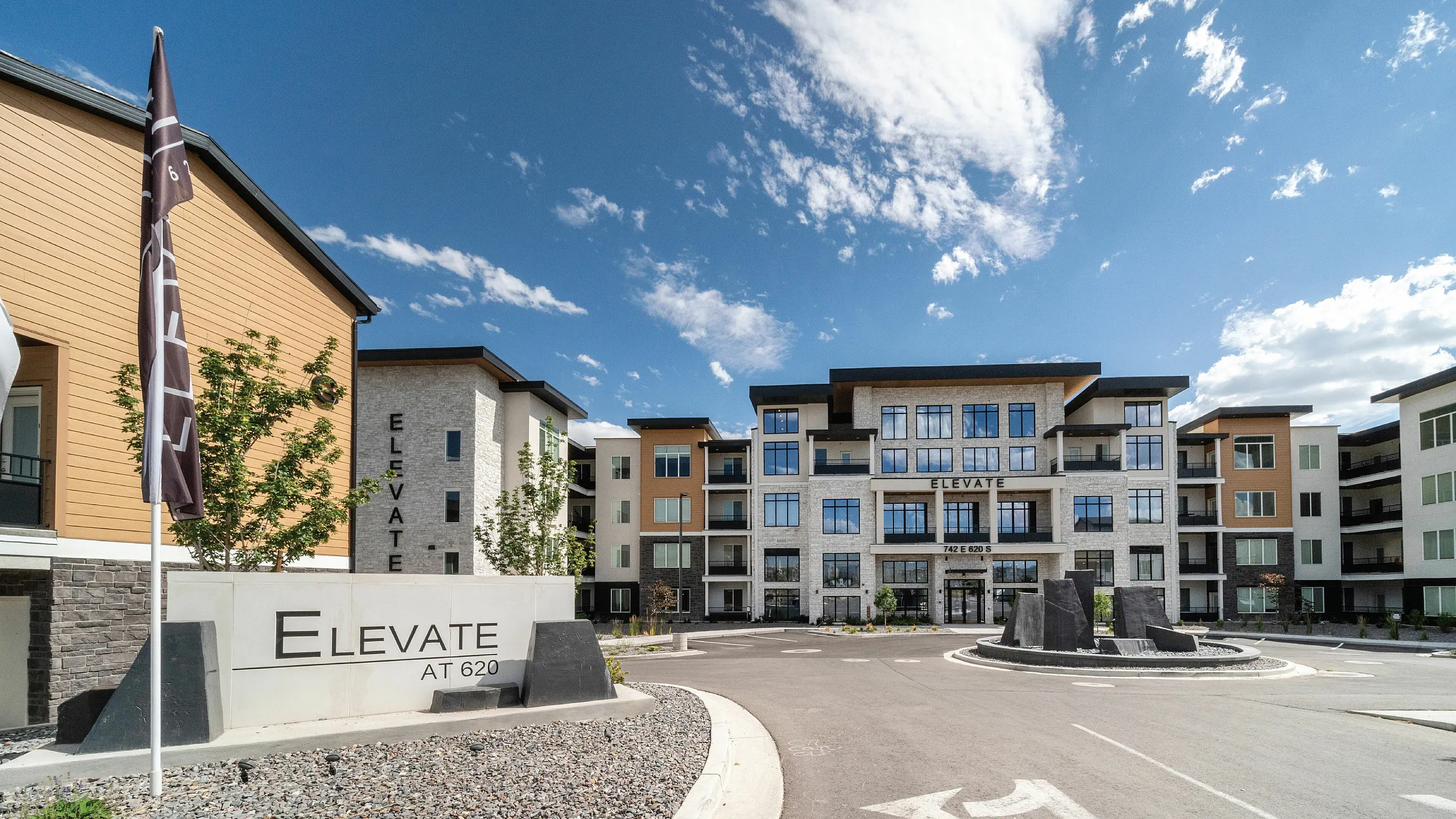 Elegant modern apartment complex with large glass windows and contemporary architecture, showcasing spacious living spaces under a bright blue sky.
