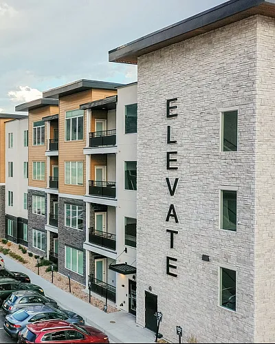 Modern apartment complex with stunning mountain views, featuring sleek architecture and ample parking spaces.