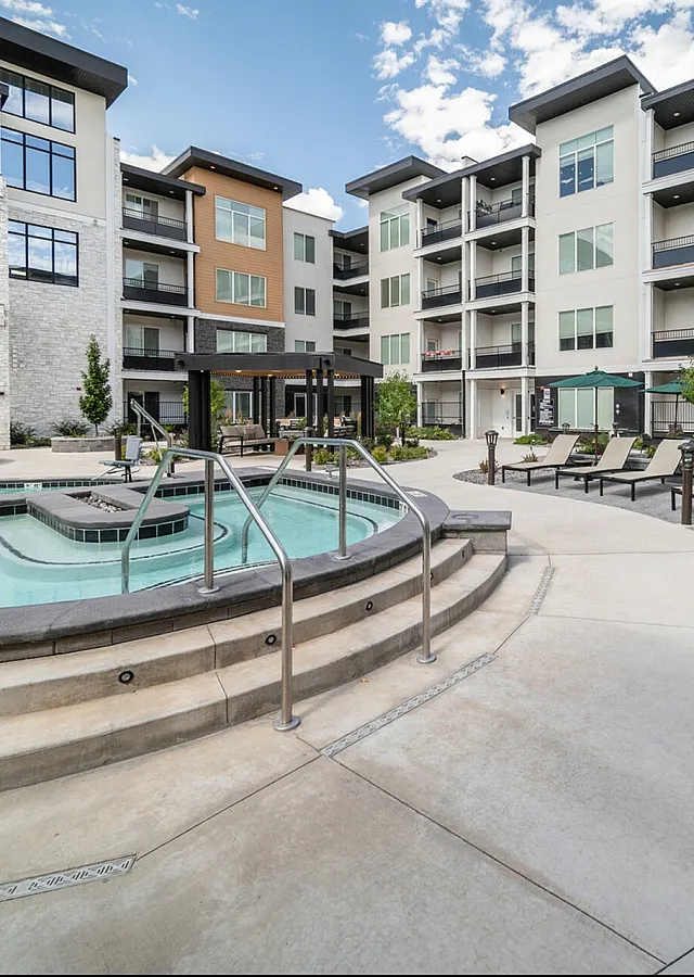 Luxurious apartment complex with resort-style pool and spacious sundeck, surrounded by modern architecture and lush landscaping.