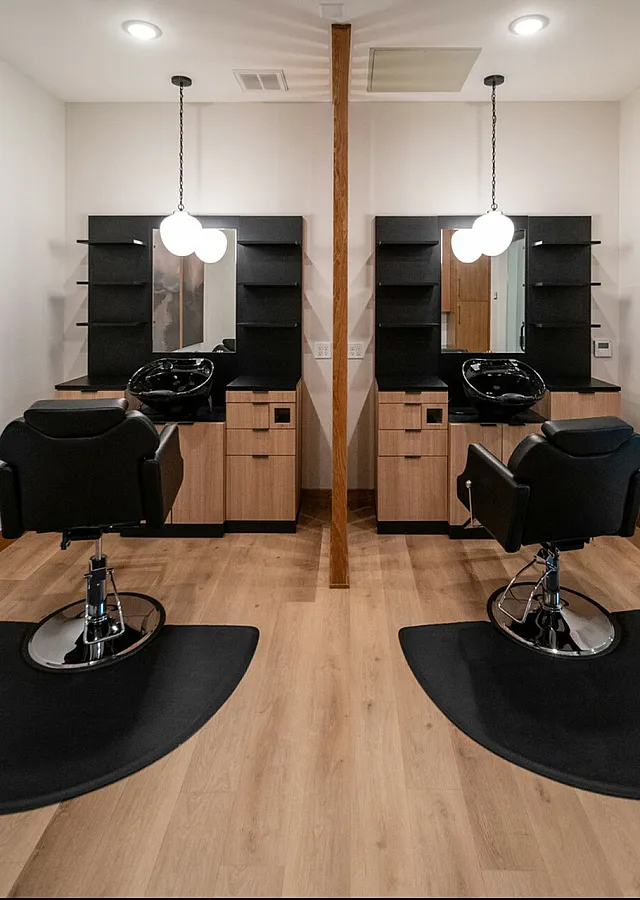 Modern salon suite with two sleek styling stations, luxurious black chairs, and elegant lighting, perfect for a sophisticated beauty experience.