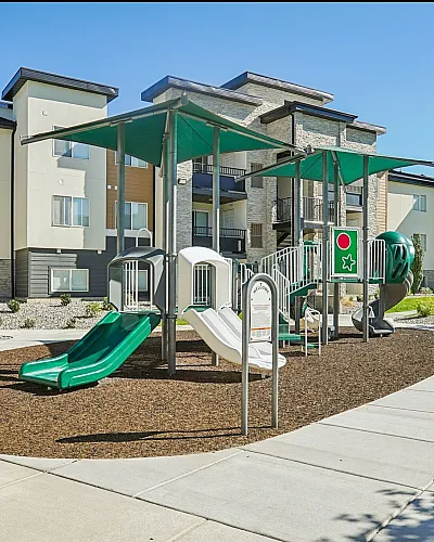 Modern apartment complex highlighted by a vibrant playground with slides and climbing structures, surrounded by lush landscaping and inviting community spaces.