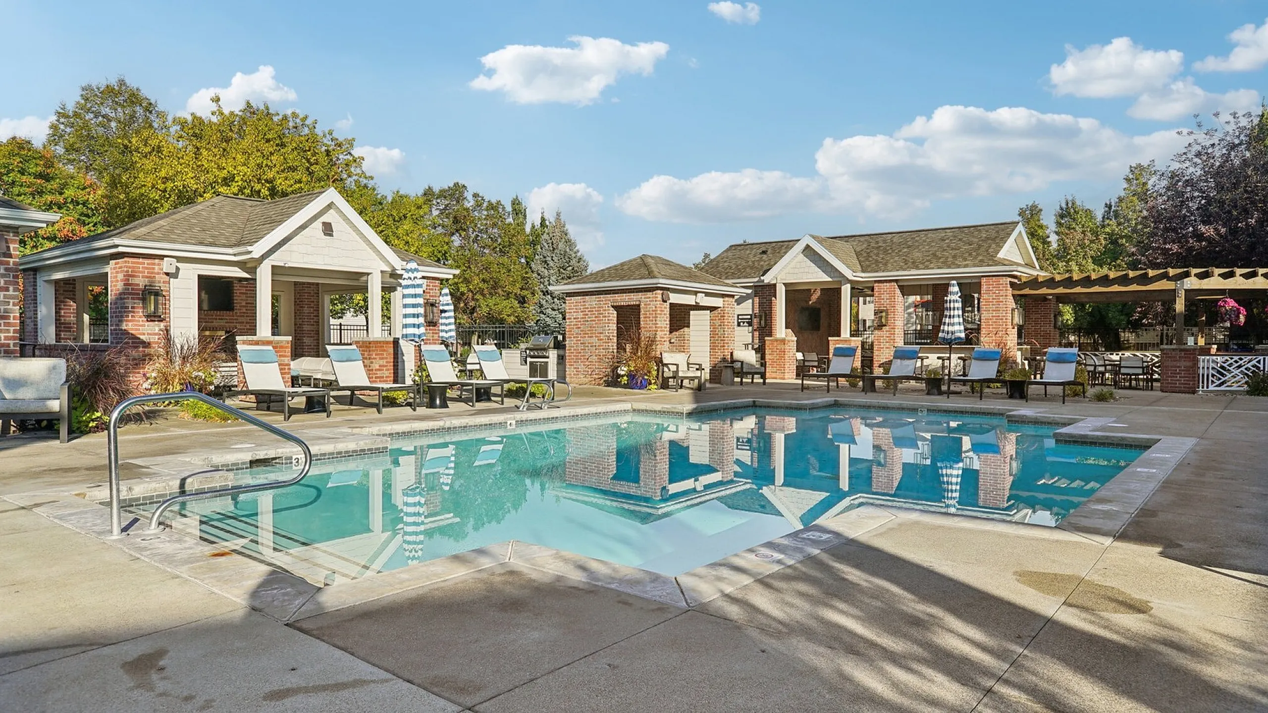 Inviting outdoor pool area featuring stylish lounge chairs and charming brick pergolas, bathed in warm sunlight, offering a perfect relaxation spot.