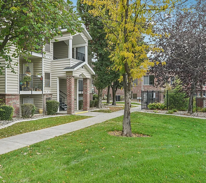 Charming apartment exterior featuring lush landscaping, mature trees, and a welcoming entrance, ideal for comfortable living.