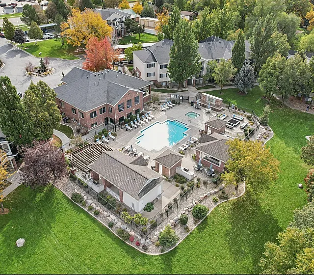 Aerial view of a lush apartment complex featuring a sparkling pool, lush green lawns, beautiful landscaping, and a cozy outdoor lounging area, ideal for tranquil living.