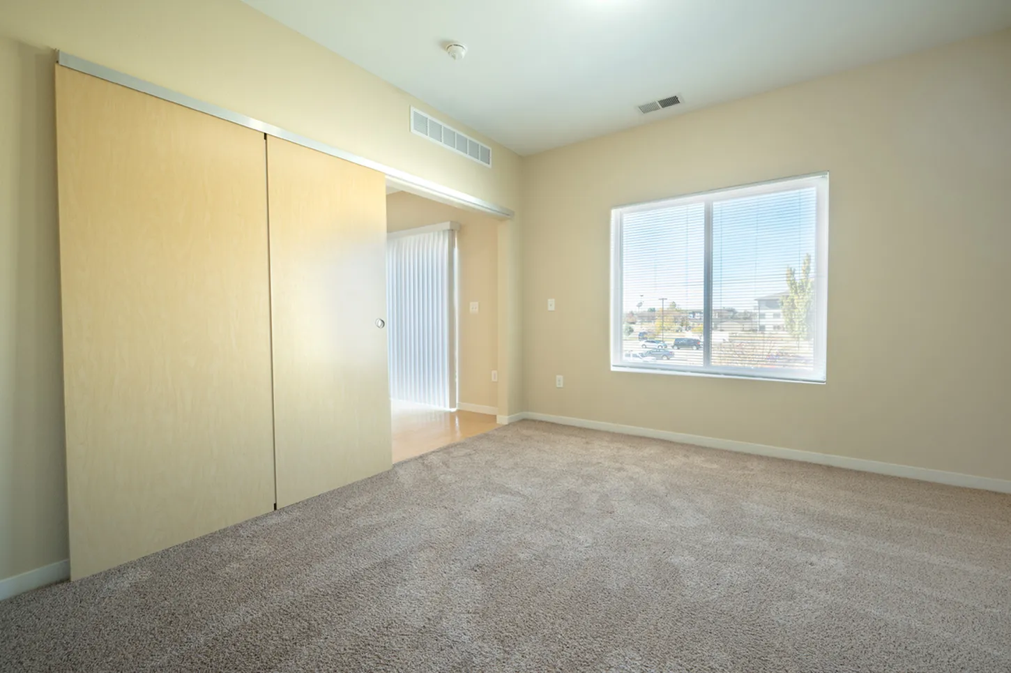 Bright bedroom with large window, plush carpet, and sliding closet doors in a modern apartment.