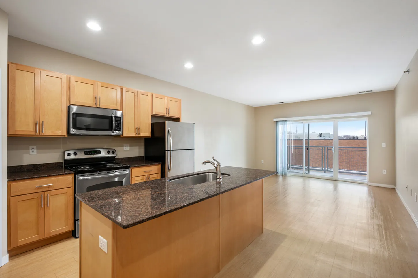 Modern open-concept kitchen with granite countertops and stainless steel appliances, leading to a bright living area with large sliding glass doors.