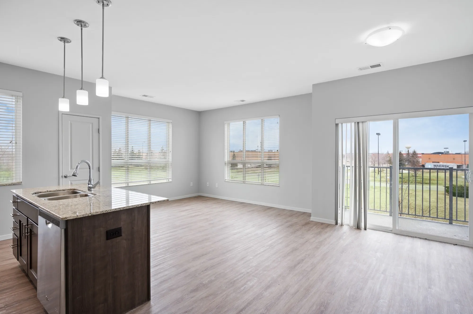 Bright, modern open-concept living space with hardwood floors, a stylish kitchen island, and large windows offering an inviting view.