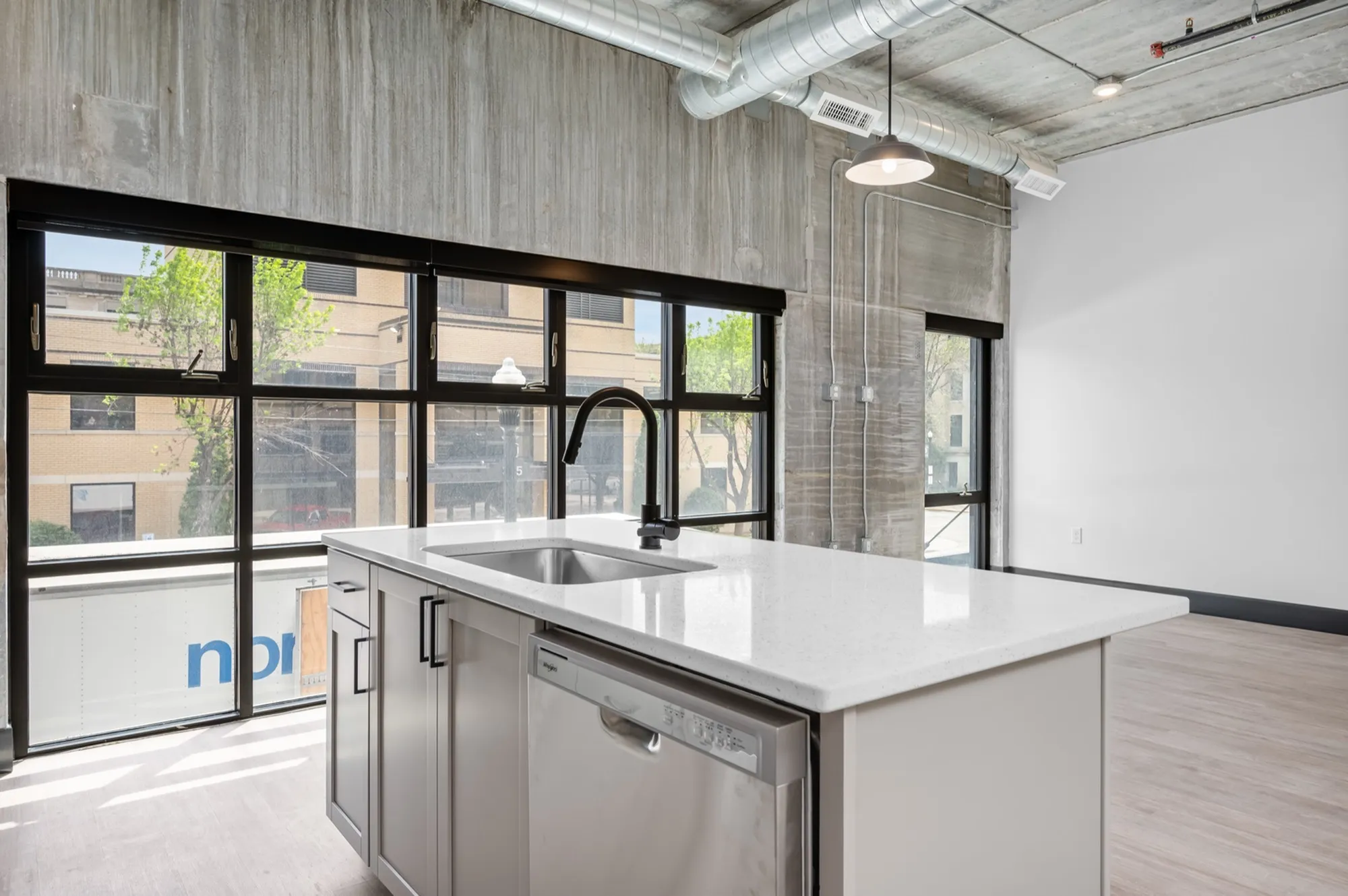 Modern industrial apartment kitchen with stunning floor-to-ceiling windows, sleek countertops, and stainless steel appliances.