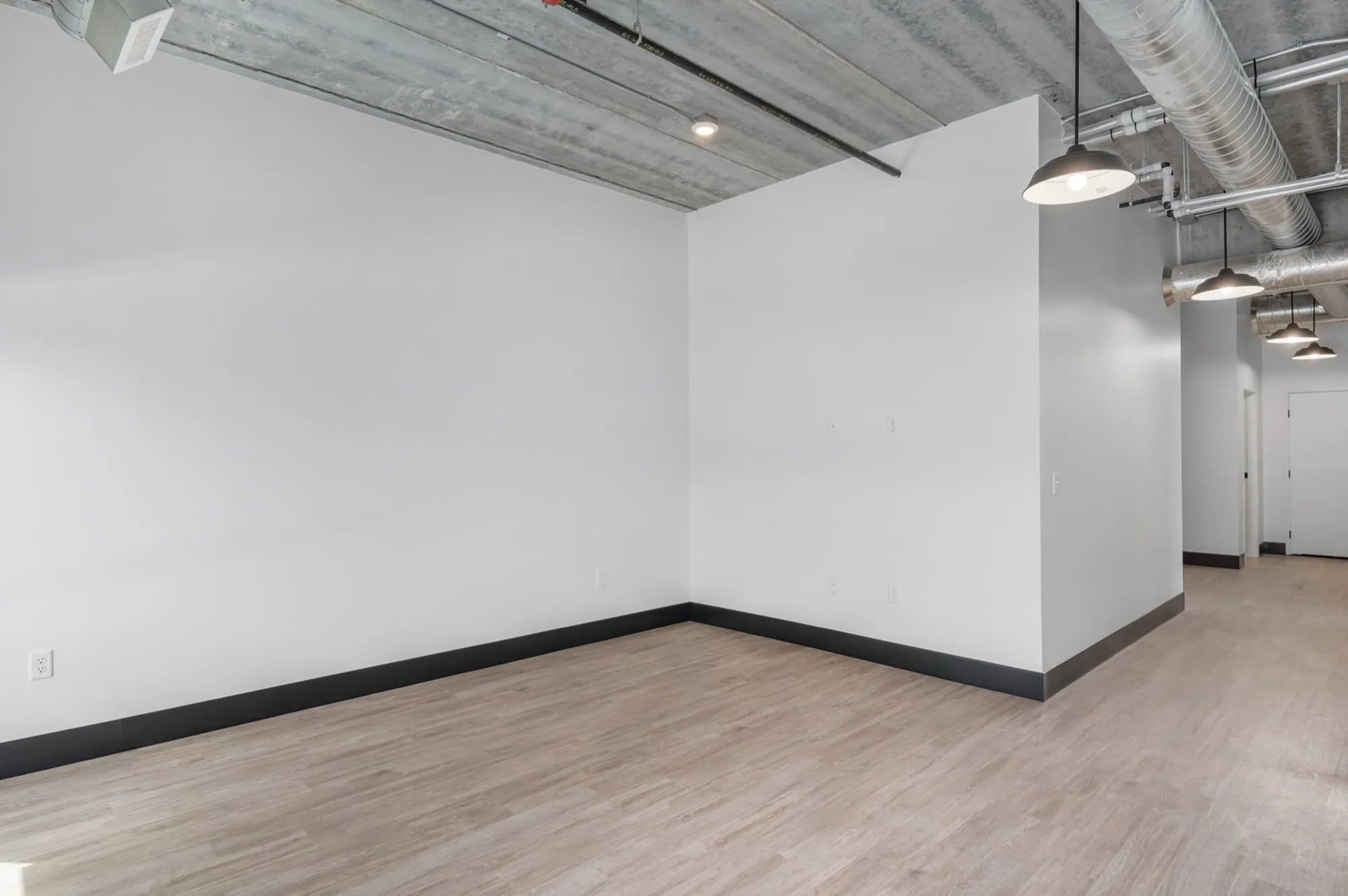 Modern industrial loft space with exposed ductwork and sleek lighting, featuring light hardwood flooring and white walls for a spacious, airy feel.
