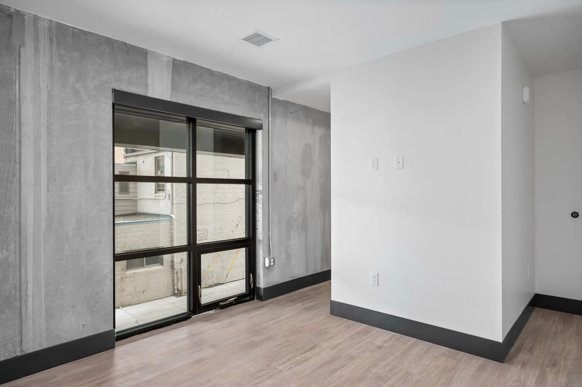 Modern apartment interior with industrial concrete walls, large windows, and sleek wooden flooring.