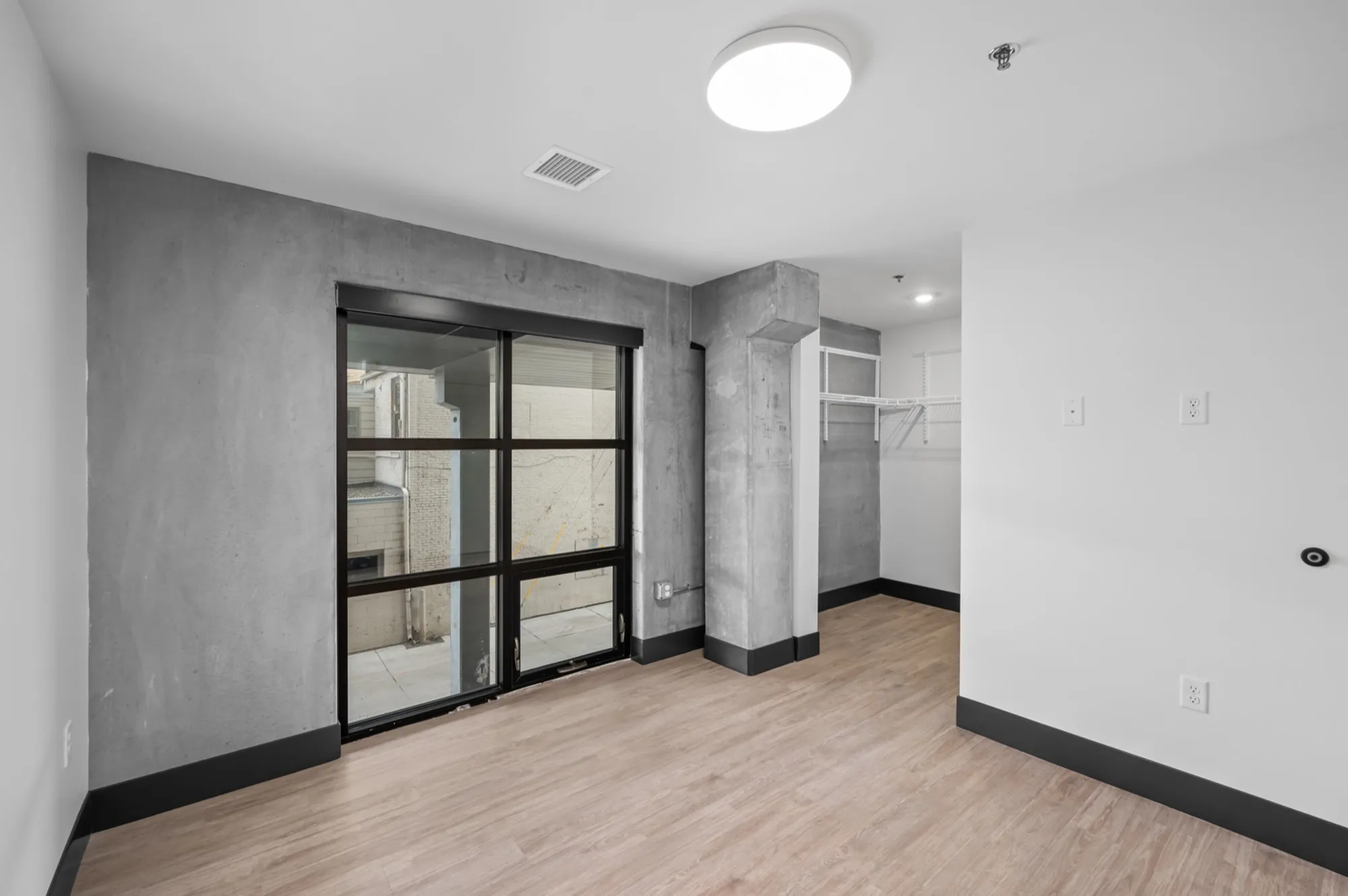 Modern apartment interior with stylish concrete accents, large glass sliding door, and built-in closet, offering a bright and open living space.
