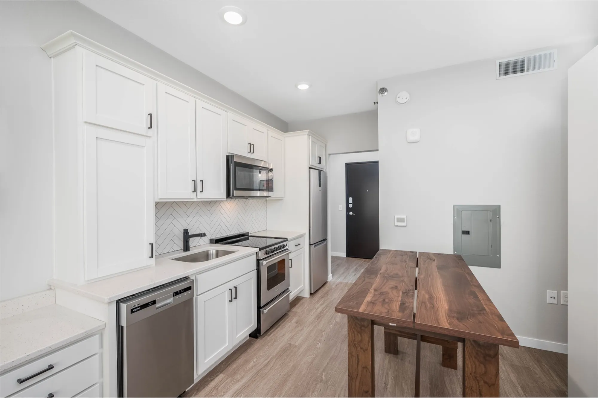 Modern kitchen with sleek white cabinetry, stainless steel appliances, and elegant wood flooring, perfect for contemporary living.