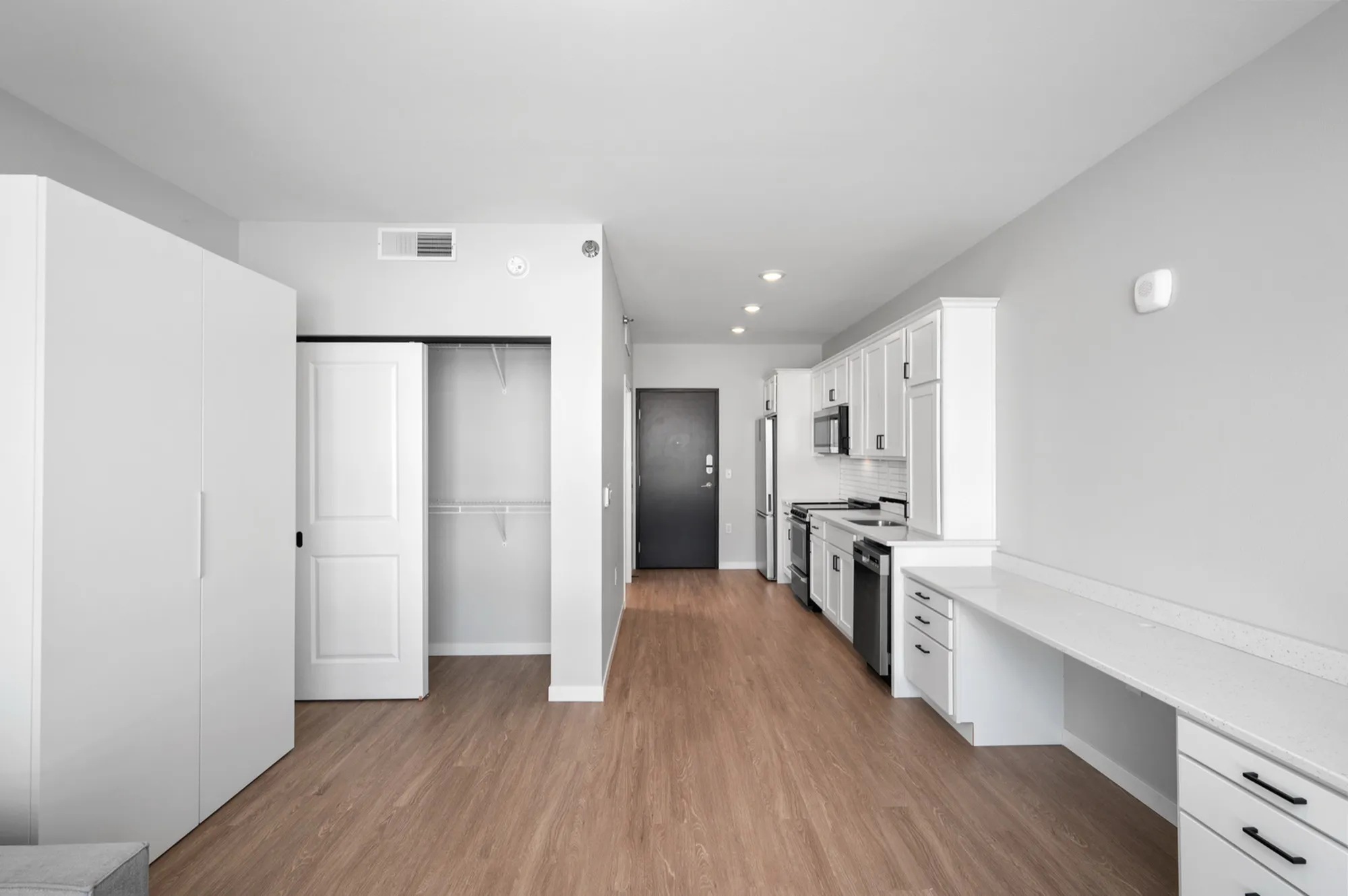 Modern apartment kitchen with sleek white cabinetry, stainless steel appliances, and elegant wood flooring.