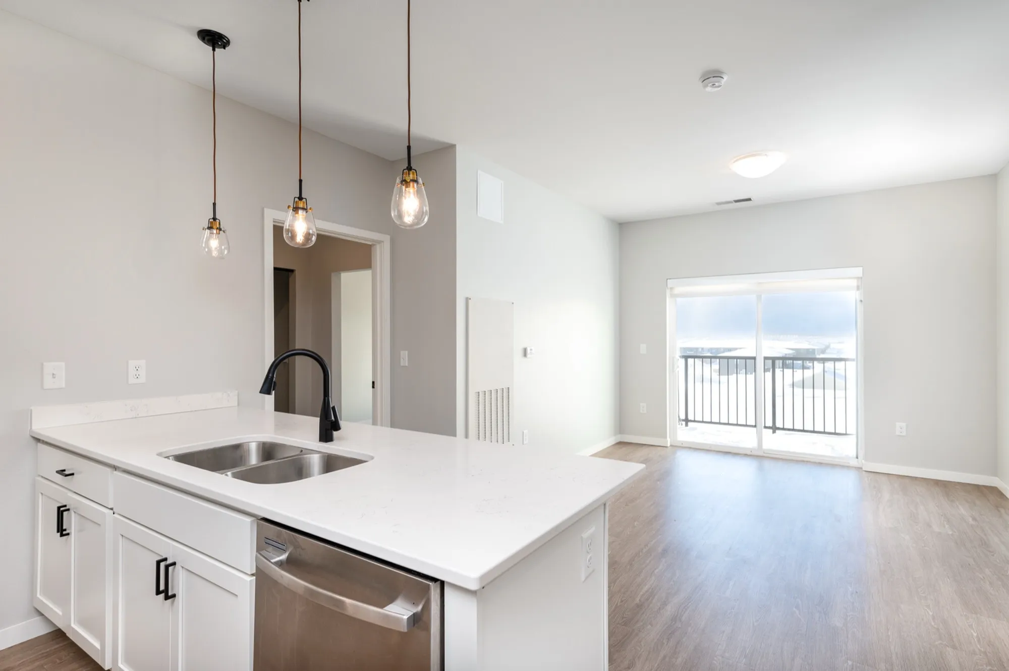 Bright modern kitchen with sleek white countertops, stylish pendant lighting, and open-concept living area leading to a balcony with scenic views.