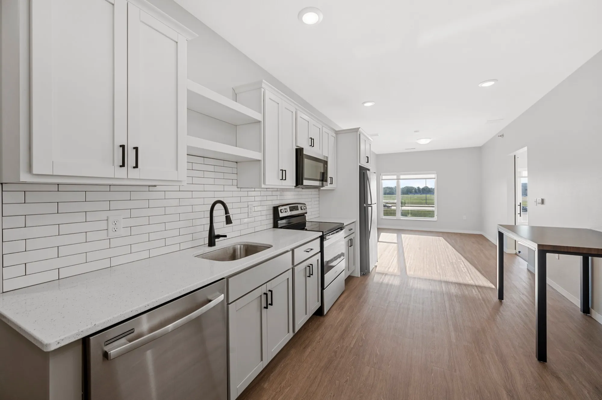 Modern kitchen with sleek white cabinetry, stainless steel appliances, and an open-concept design flowing into a sunlit living area.