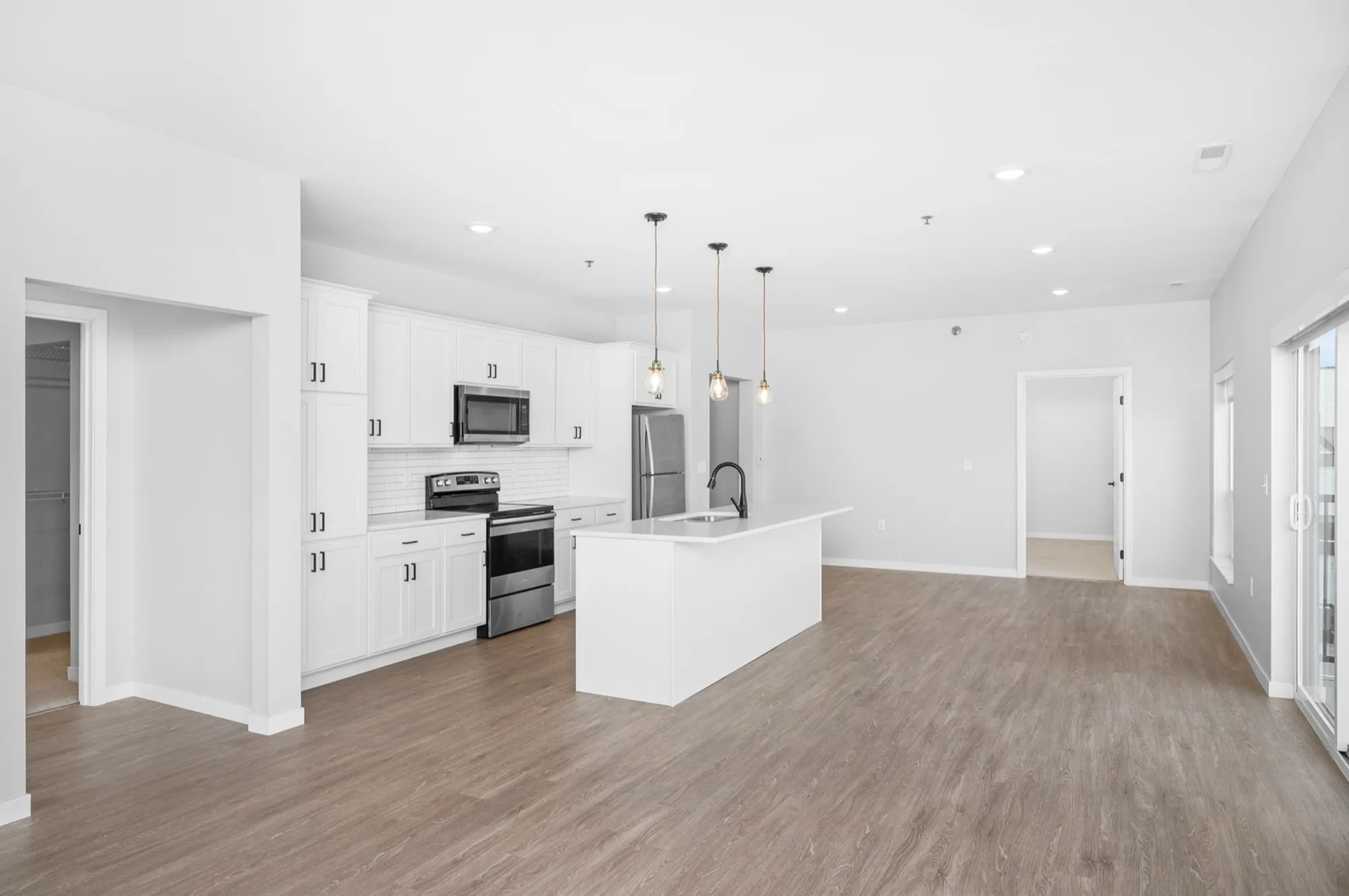 Modern open-concept kitchen and living area with sleek white cabinetry, stainless steel appliances, and elegant pendant lighting.