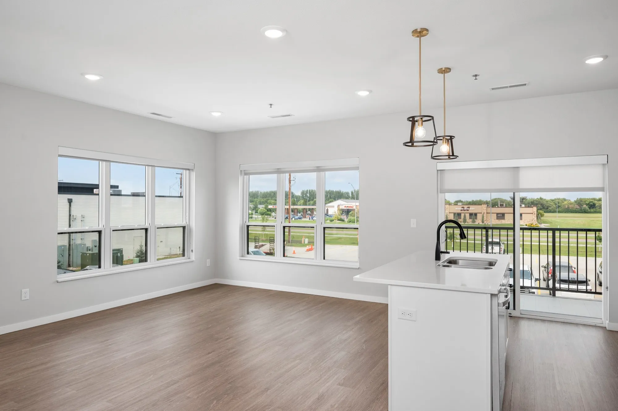 Bright, open-concept apartment with floor-to-ceiling windows, modern lighting, and a stylish kitchen island with sink, overlooking peaceful views.