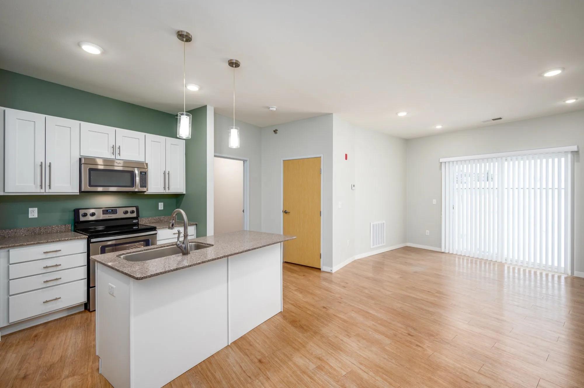 Modern open-plan kitchen and living area featuring sleek white cabinetry, stainless steel appliances, and elegant wood flooring.