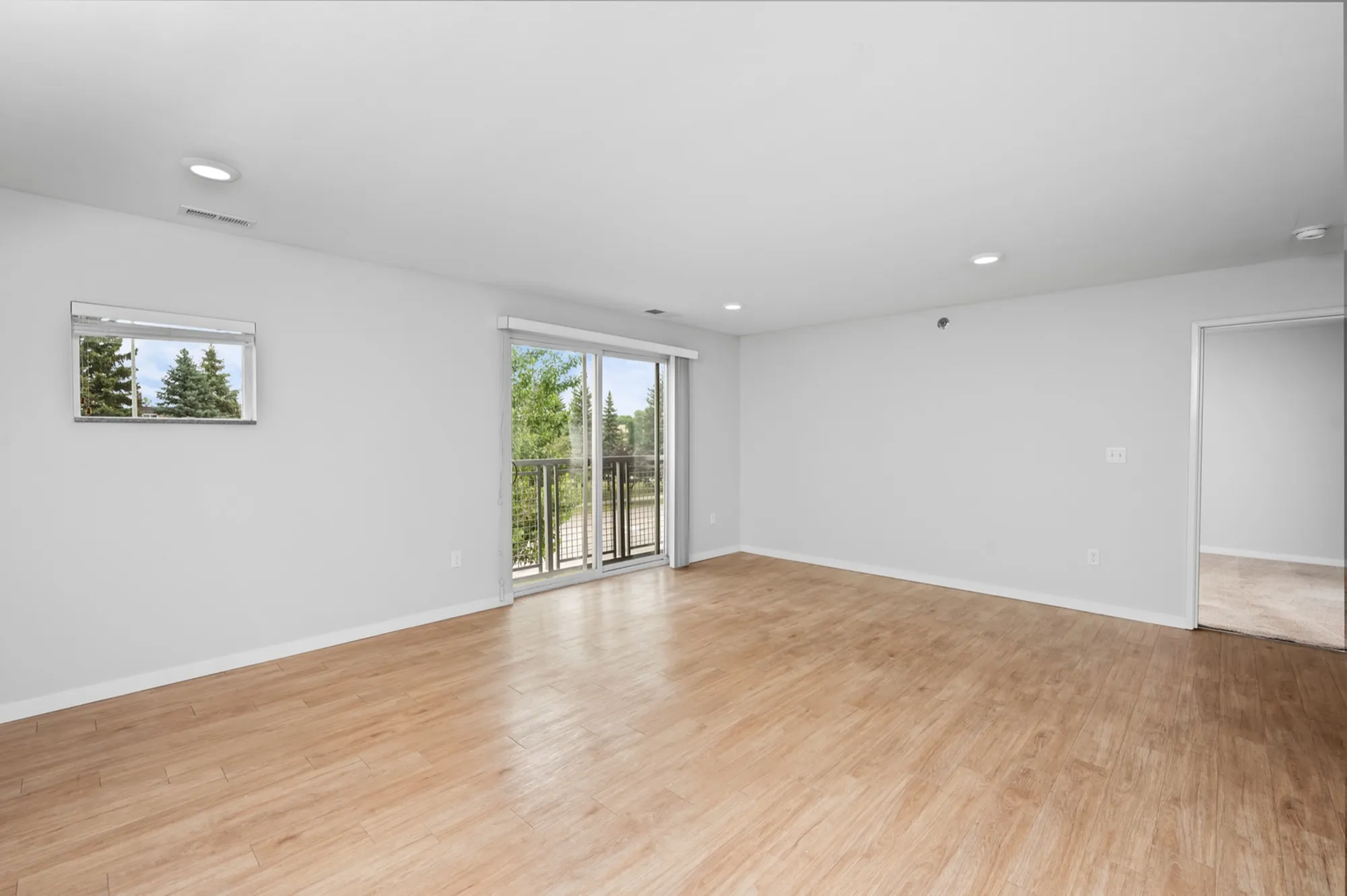Bright living room with elegant hardwood floors, large sliding glass doors leading to a balcony, and a neutral color palette for a spacious feel.