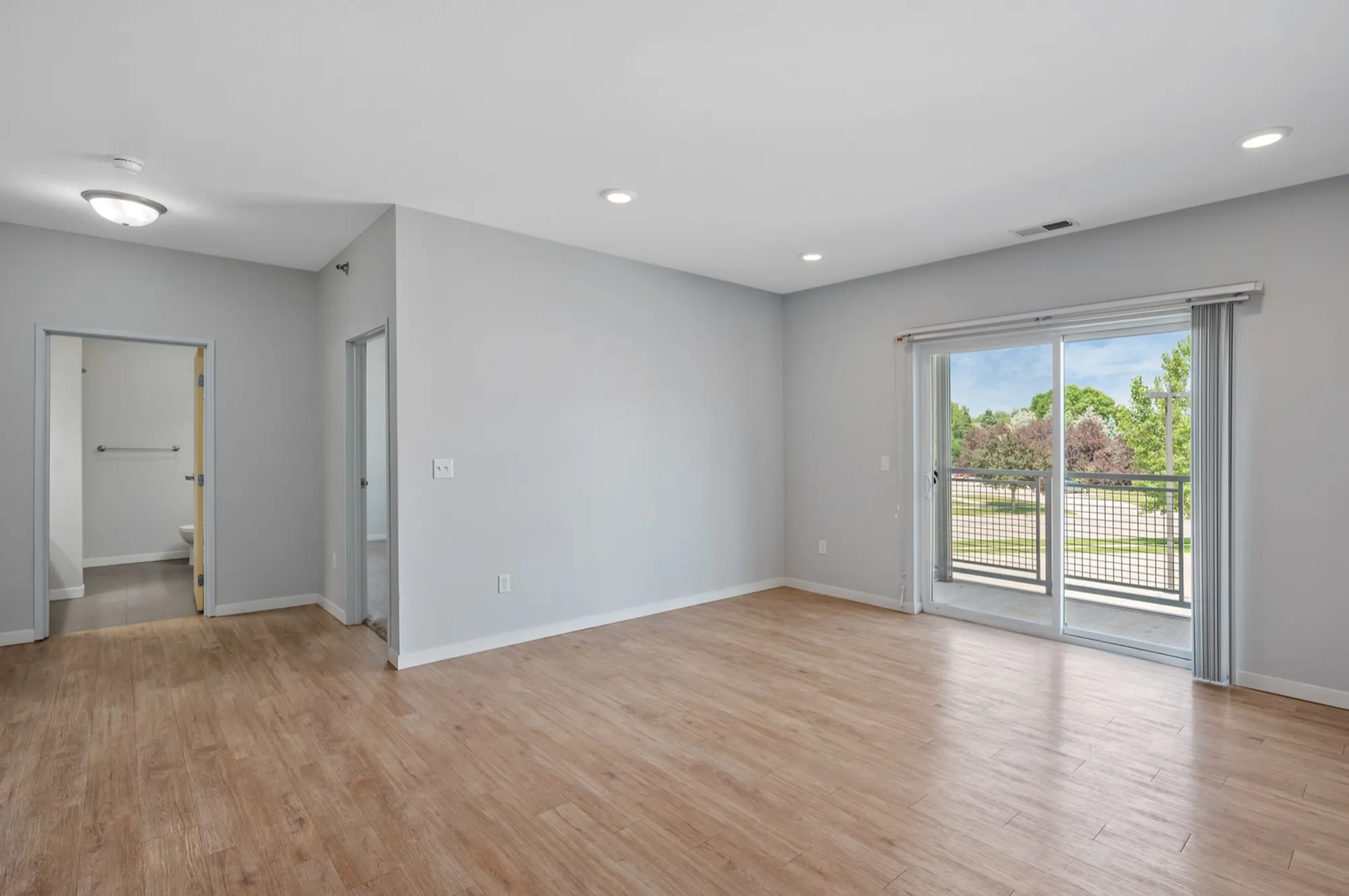 Bright and airy living space with large sliding glass doors leading to a balcony, featuring modern hardwood floors and soft gray walls.
