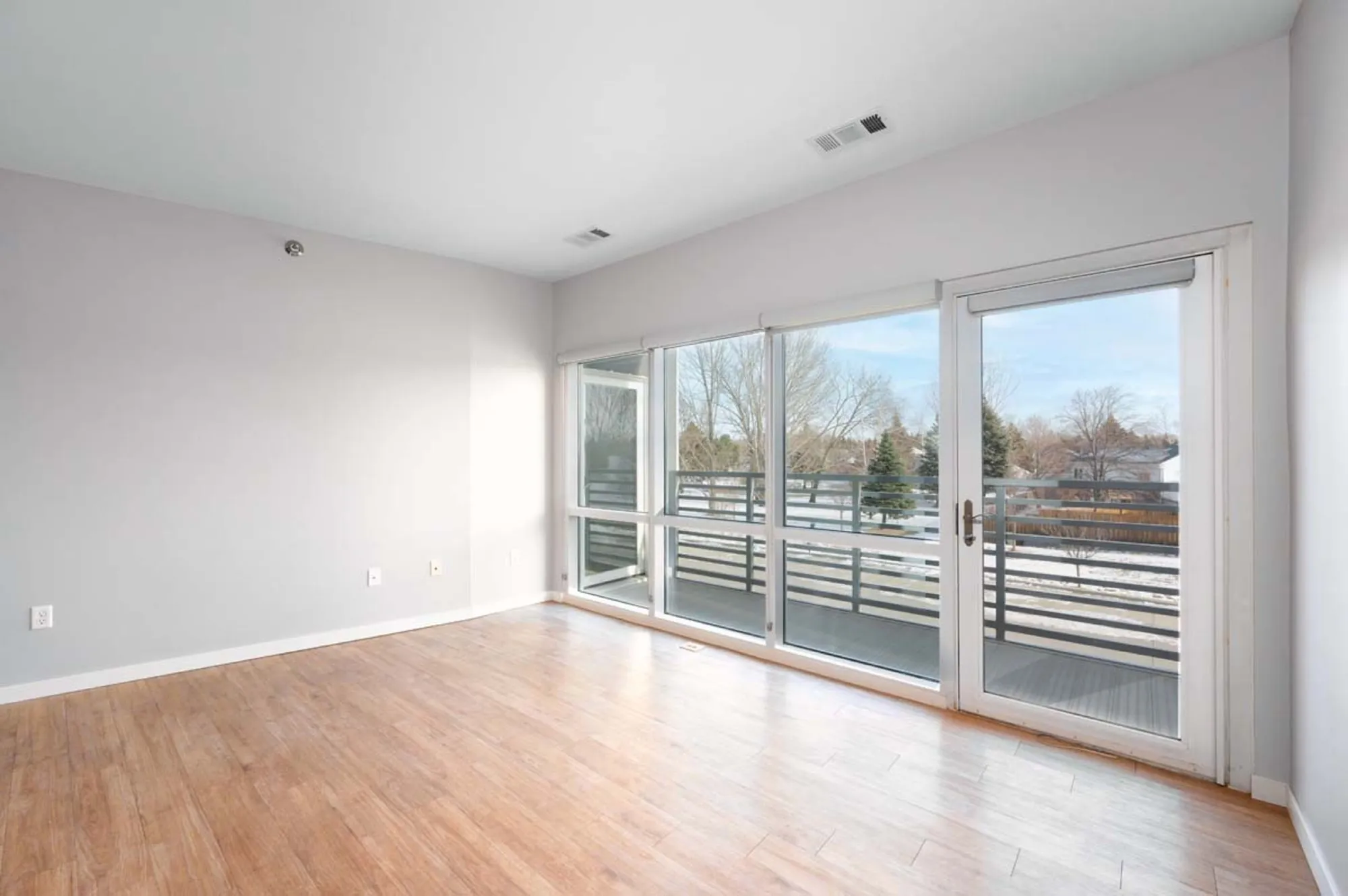 Bright and airy empty room with large windows and hardwood flooring, leading to a spacious balcony with scenic views.