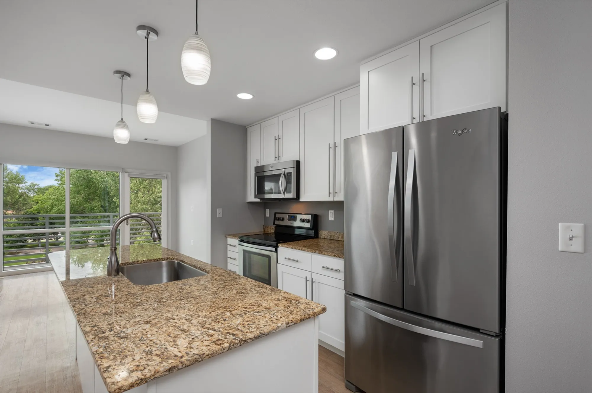 Modern kitchen with granite countertops, stainless steel appliances, and pendant lighting, overlooking a scenic balcony view.