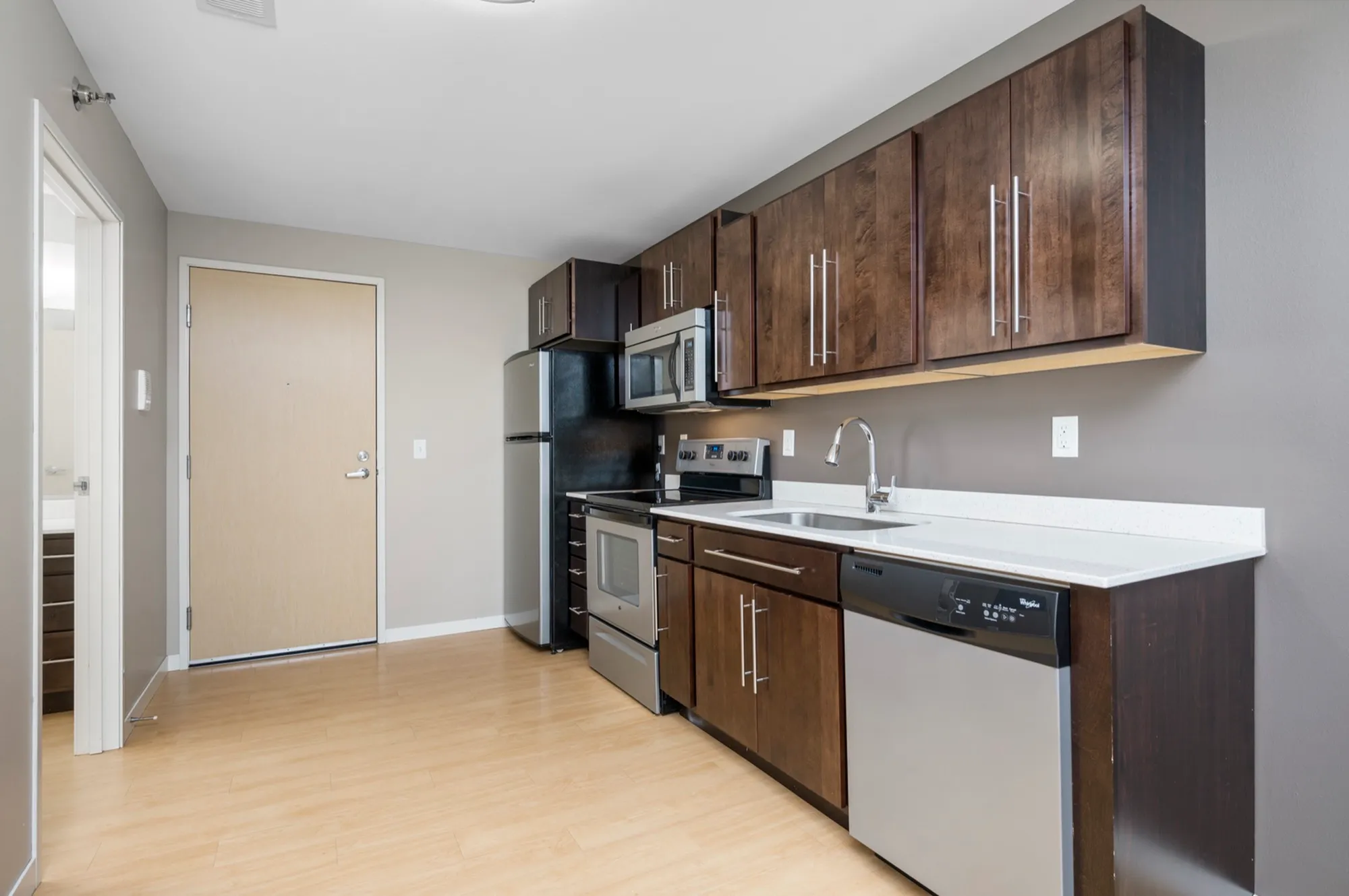 Modern kitchen with sleek wooden cabinets, stainless steel appliances, and bright laminate flooring.