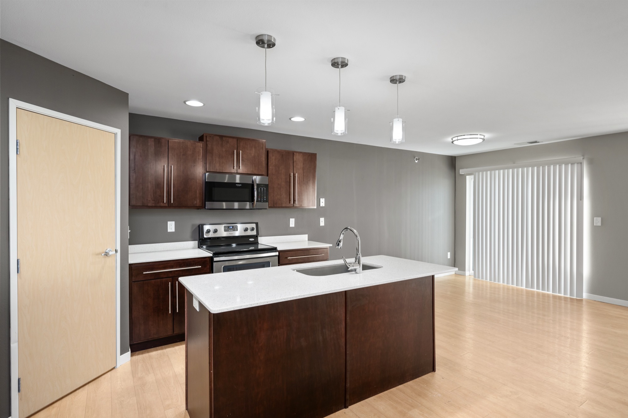 Modern apartment kitchen with sleek dark wood cabinets, a spacious island, stainless steel appliances, and elegant pendant lighting.