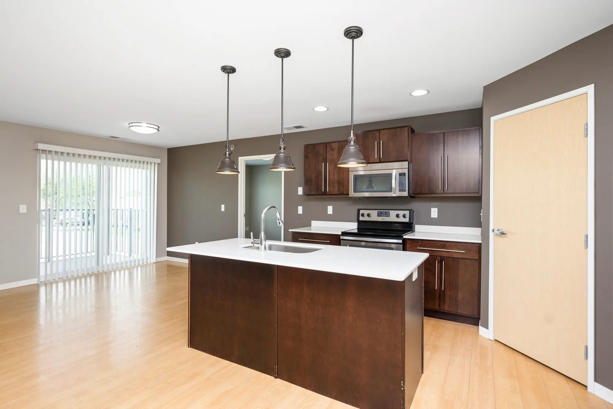 Modern kitchen with sleek countertops, stainless steel appliances, and elegant pendant lighting, opening to a bright living area with sliding glass doors.
