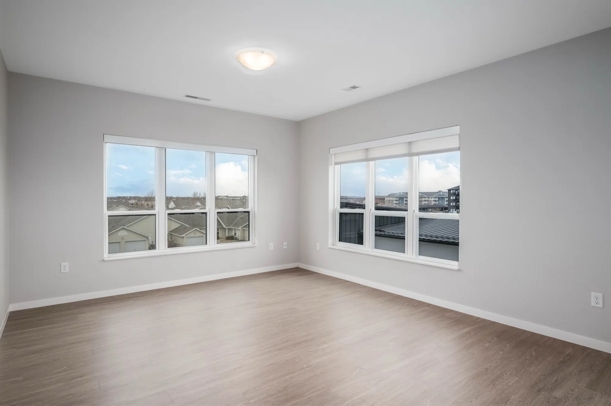 Bright room with large windows offering scenic views, featuring sleek hardwood floors and soft neutral walls, ideal for a modern living area.