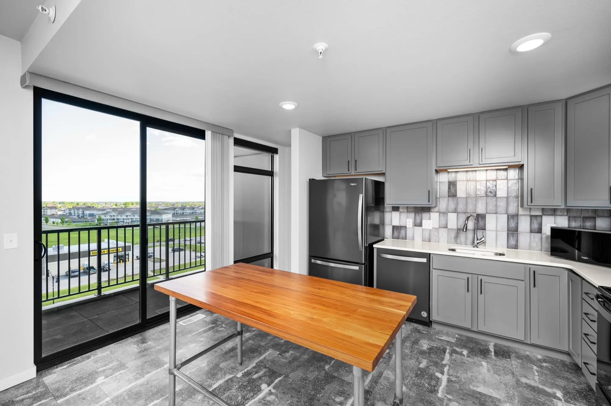 Modern kitchen with sleek gray cabinetry, stainless steel appliances, a wooden island, and large windows overlooking a vibrant cityscape.