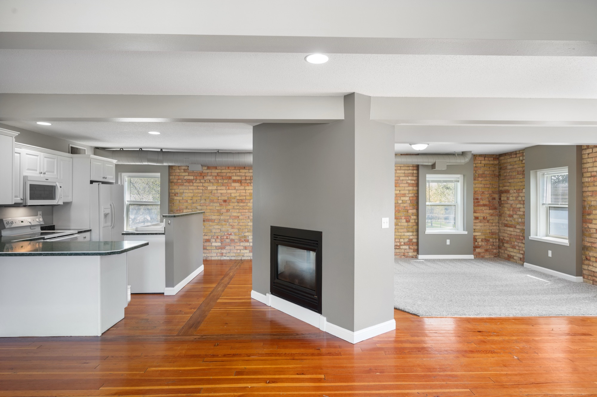 Charming open-concept living space with hardwood floors, modern kitchen, and exposed brick accents.