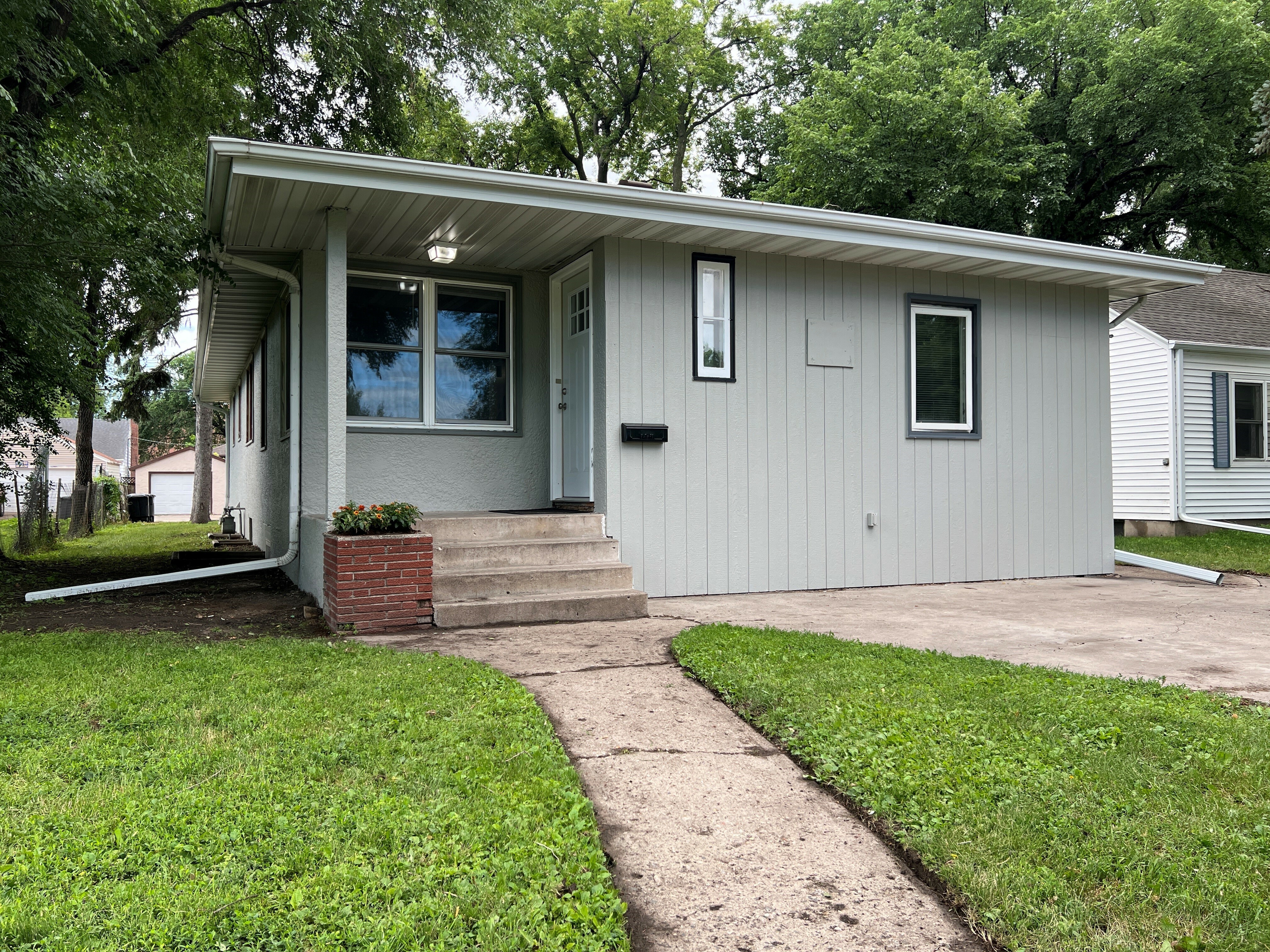 Charming single-story home with a cozy front porch, surrounded by lush greenery, perfect for serene living.