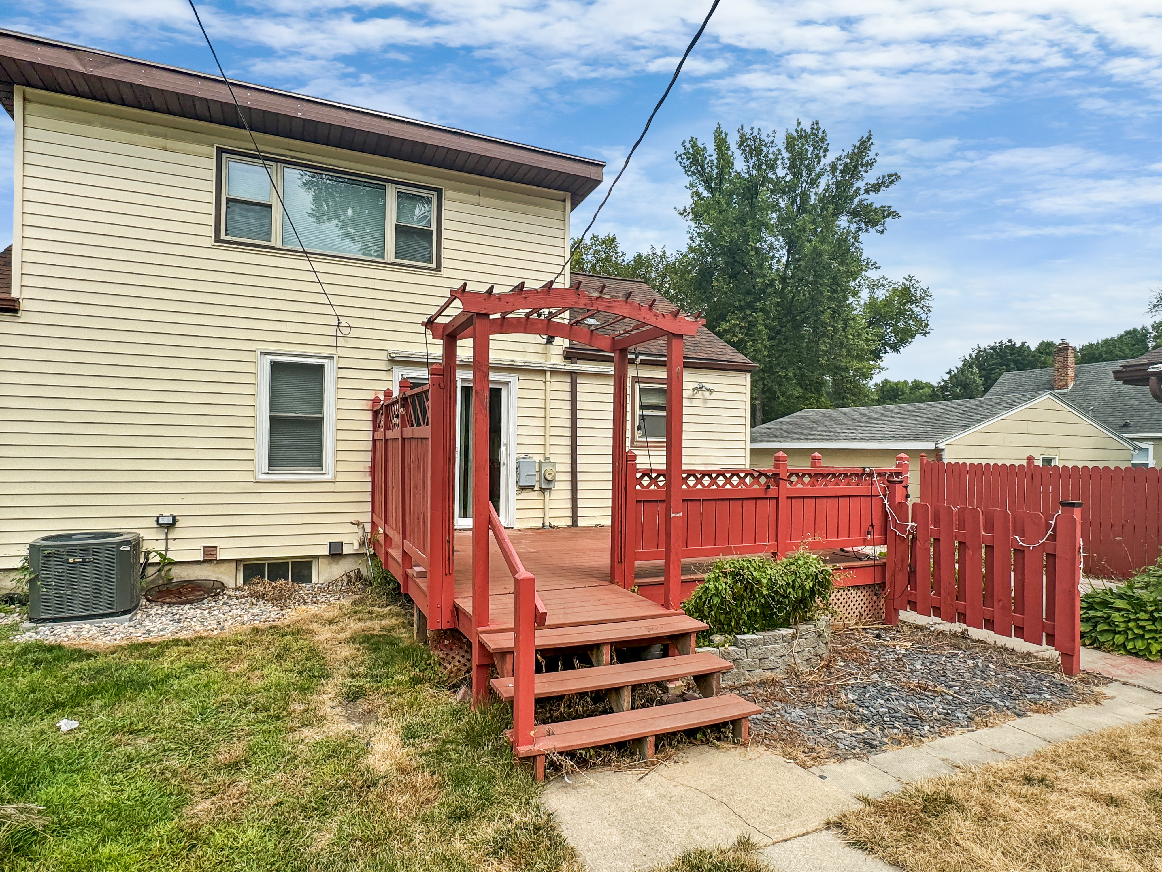 Charming backyard with a red wooden deck and pergola, perfect for outdoor gatherings and relaxation.