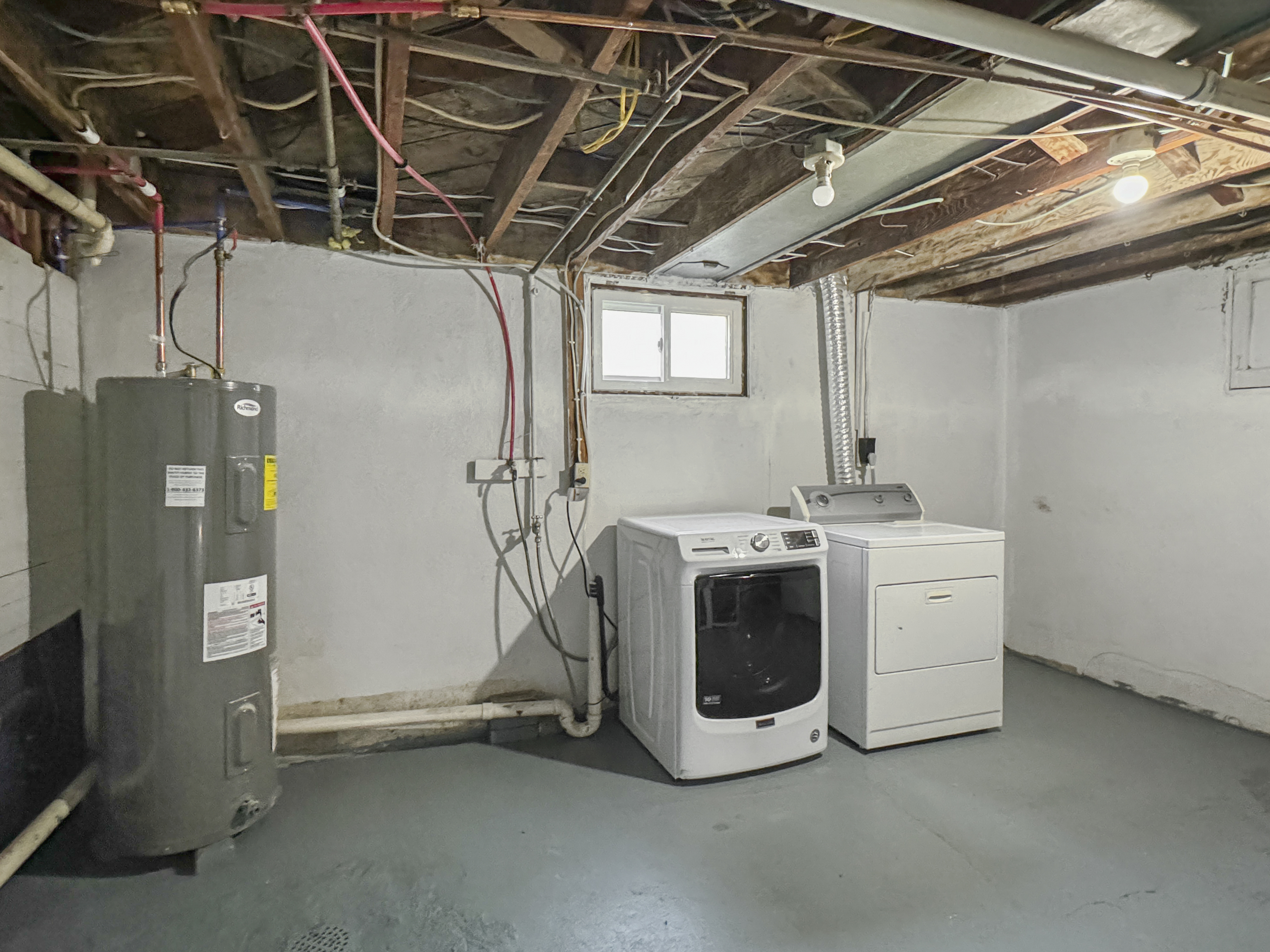 Spacious basement laundry room with modern washer, dryer, and hot water heater, showcasing ample space and potential for customization.