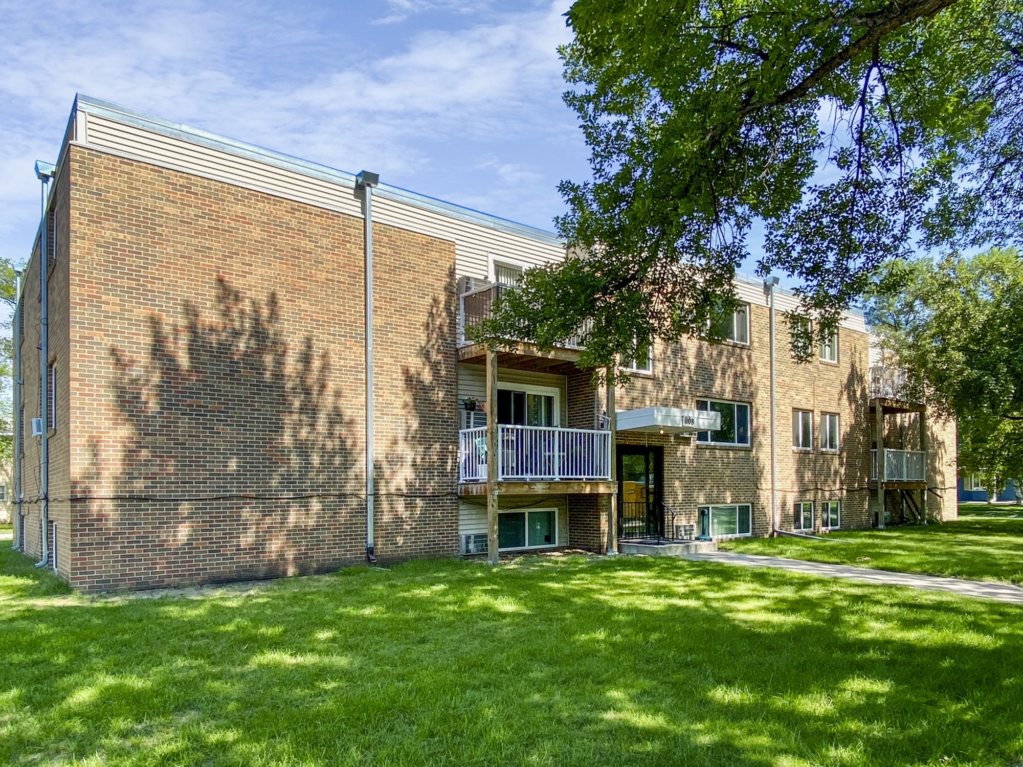 Charming brick apartment building with balconies and lush green lawn under a clear blue sky.
