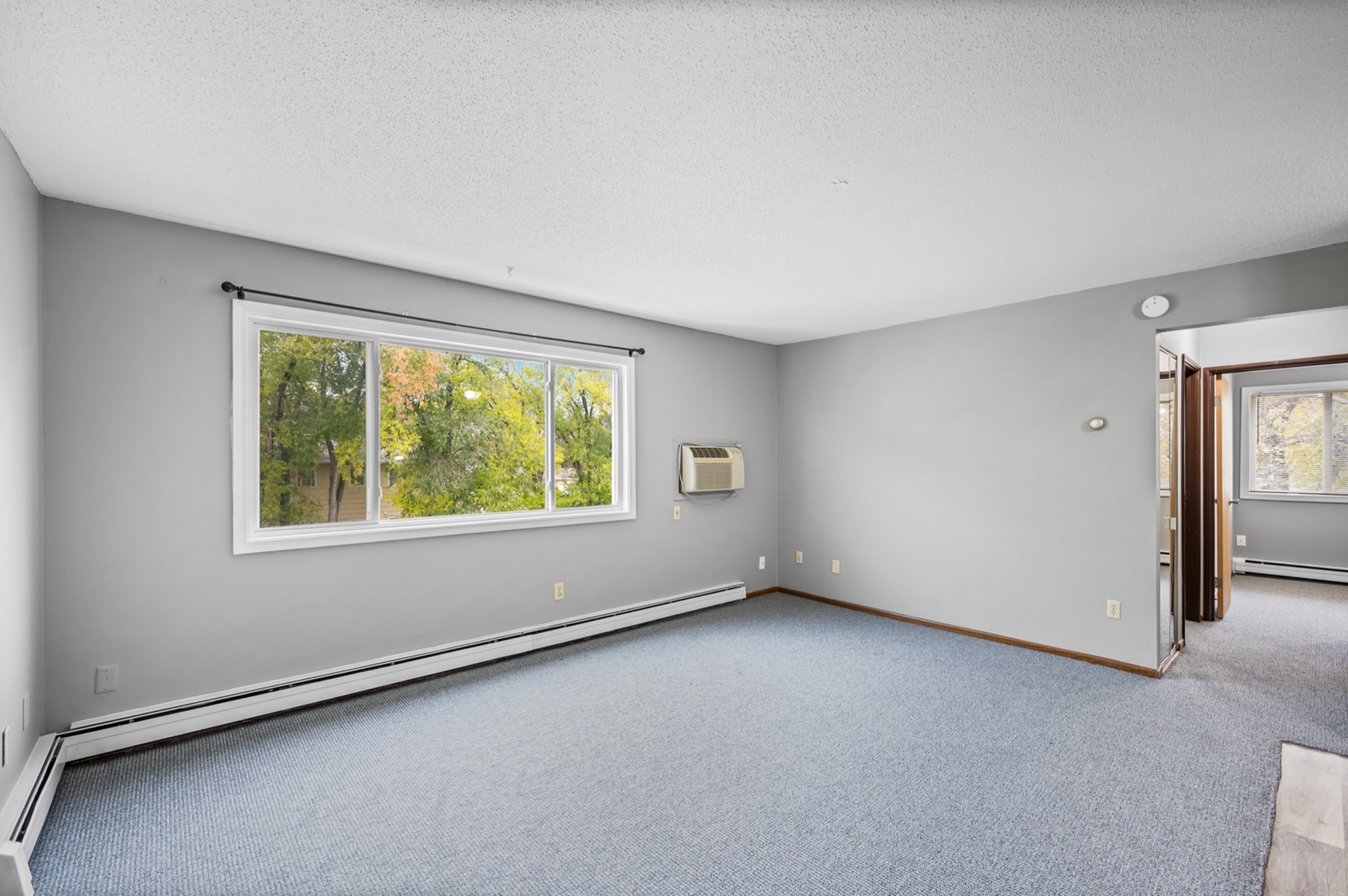 Bright, spacious living area with large window offering a scenic view, featuring an air conditioning unit for comfortable living.