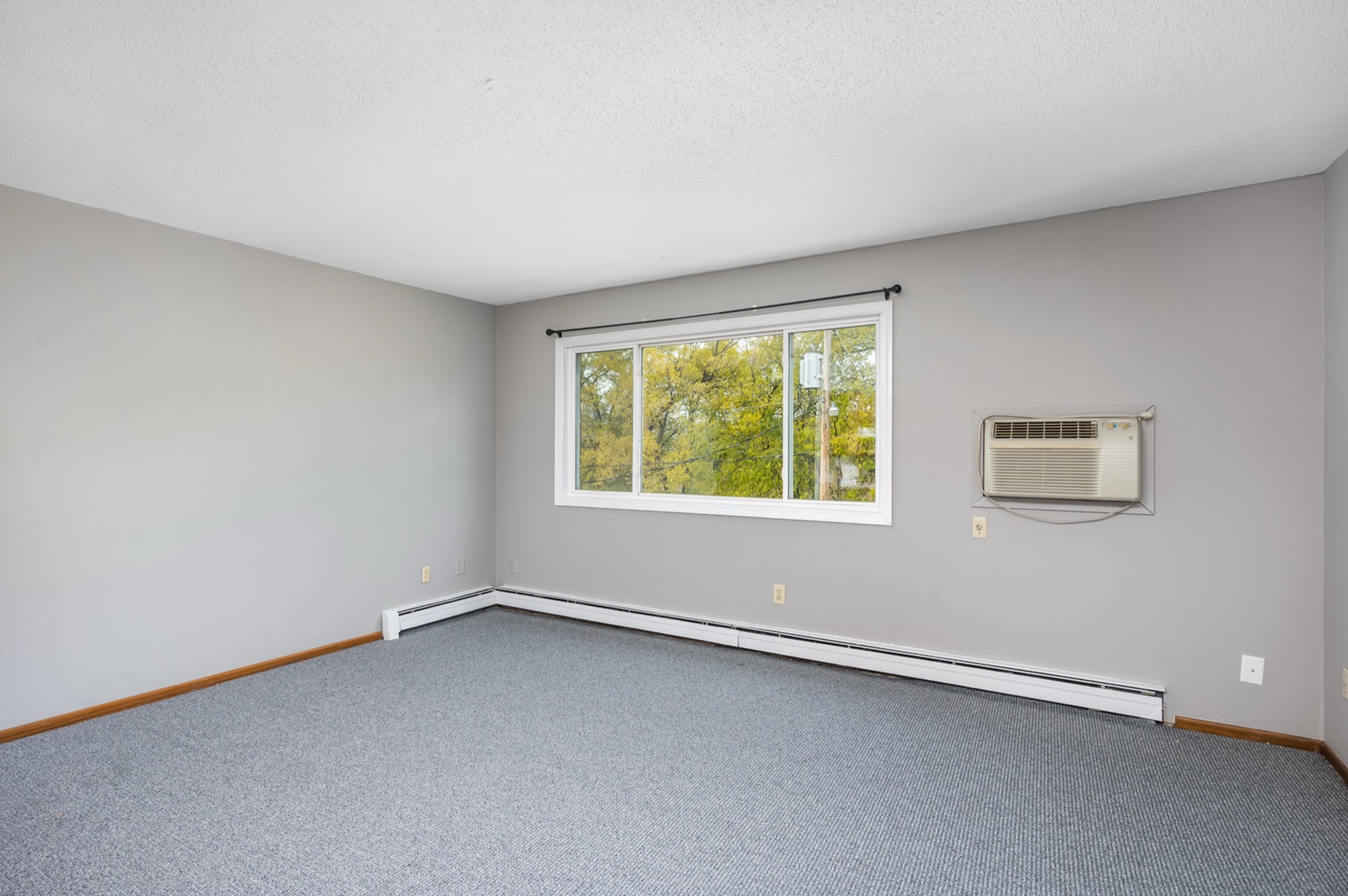 Bright and spacious room with large window and air conditioning unit, ideal for cozy living.