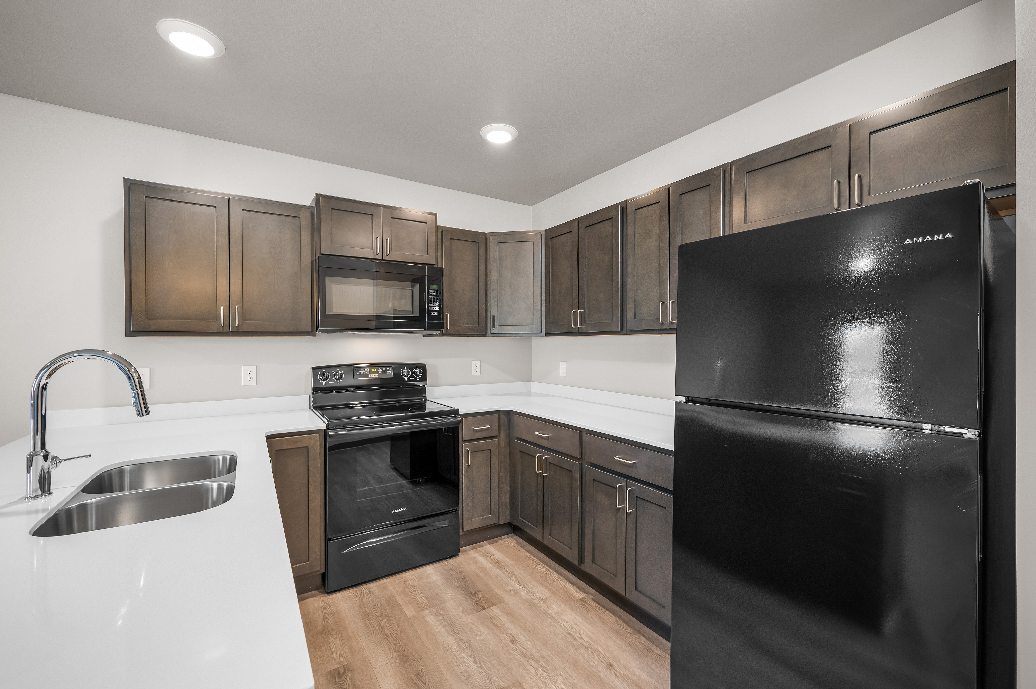 Modern kitchen with sleek black appliances, elegant dark wood cabinets, and a spacious white countertop.