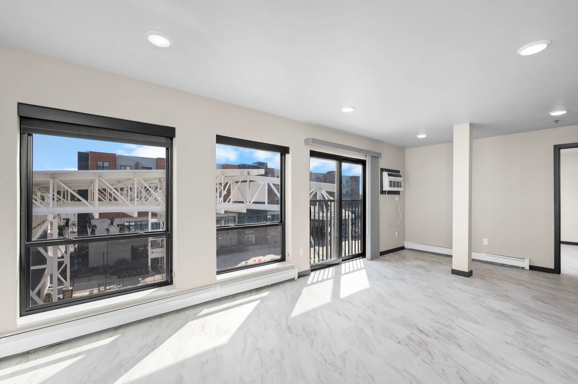 Bright modern apartment living area featuring large windows, sliding glass doors, and sleek flooring with city views.