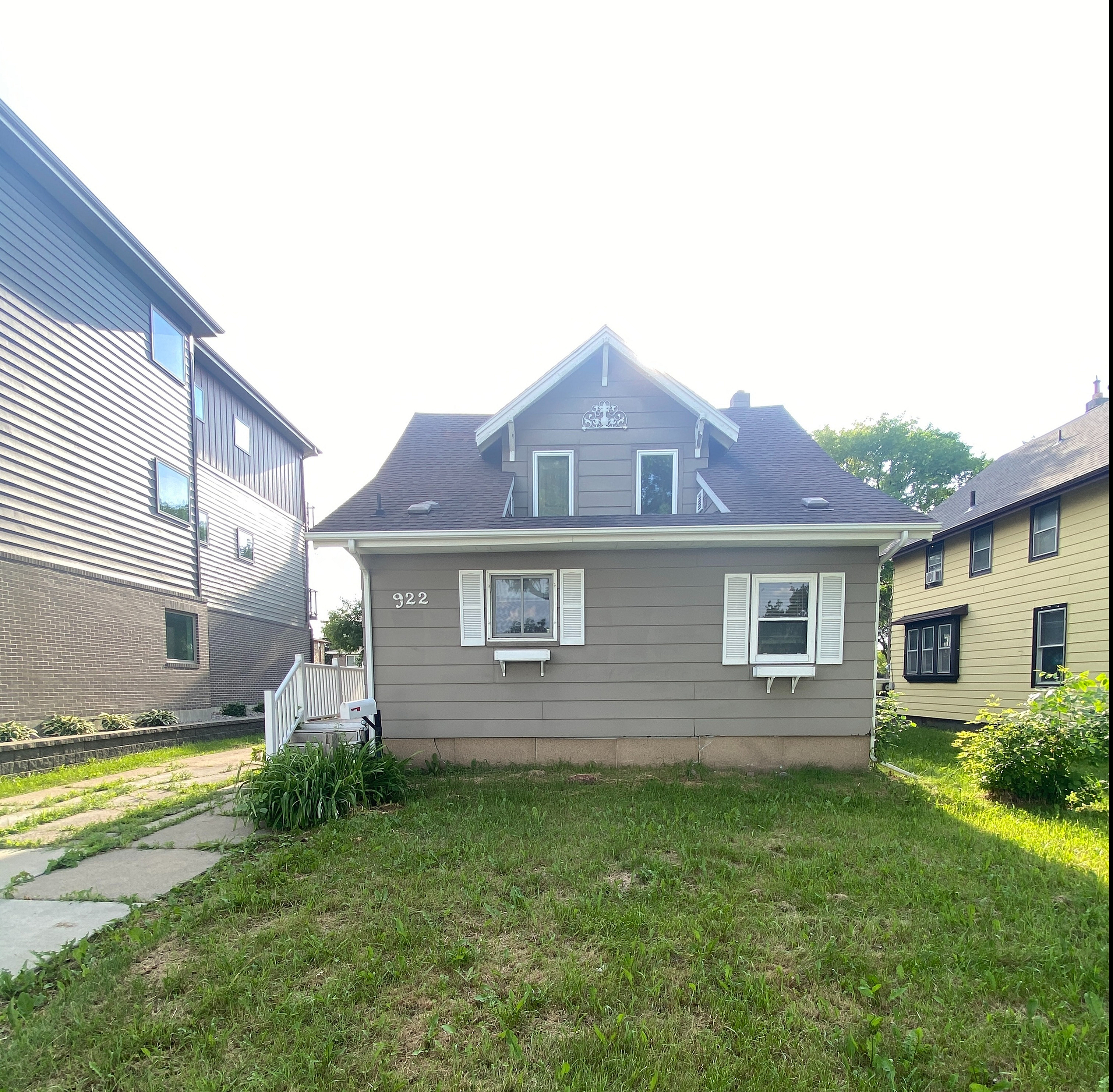Charming two-story house with gray siding, featuring a green lawn and cozy front entrance.