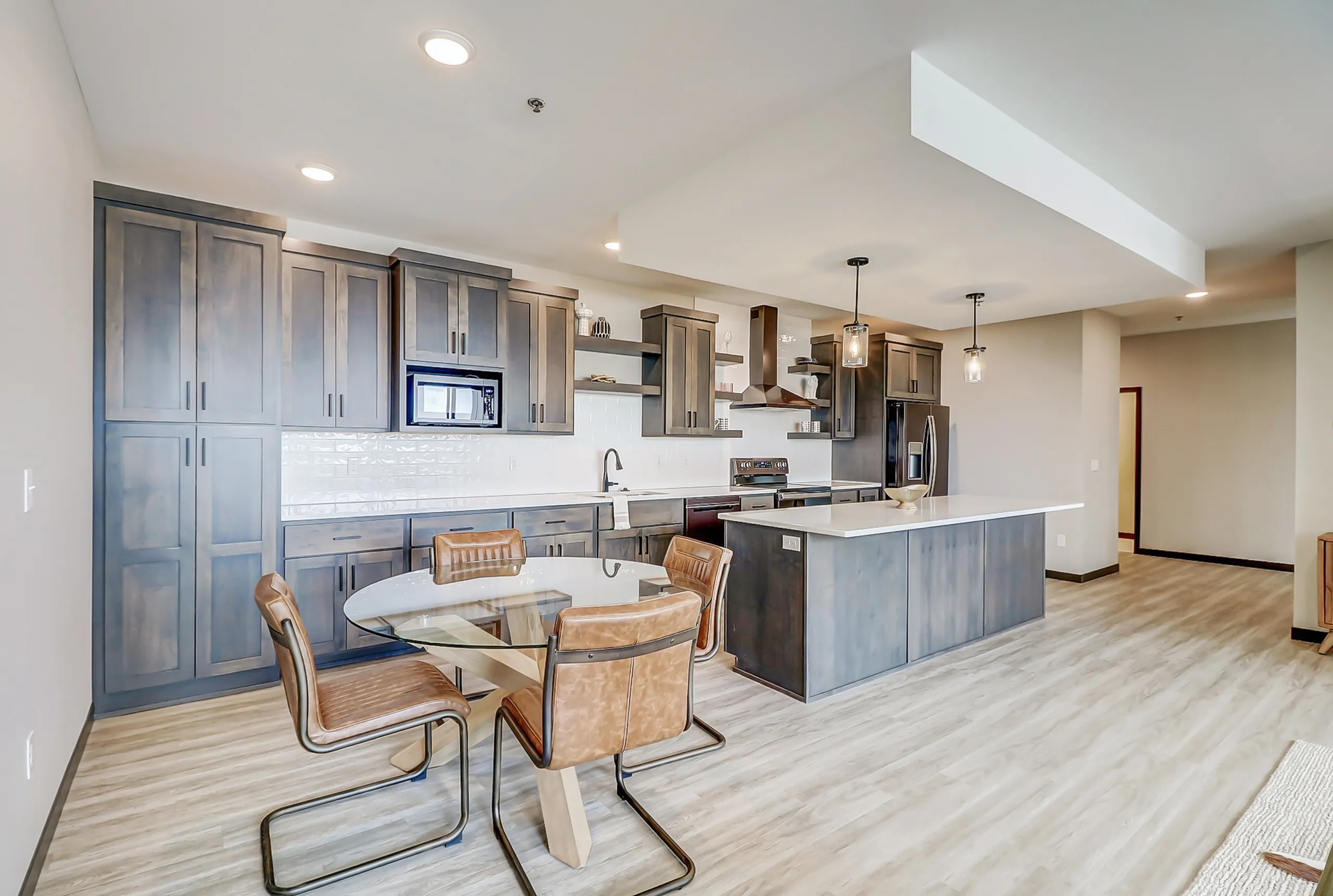 Sleek modern kitchen with dark cabinetry, stainless steel appliances, and open dining area featuring a glass-top table and leather chairs.