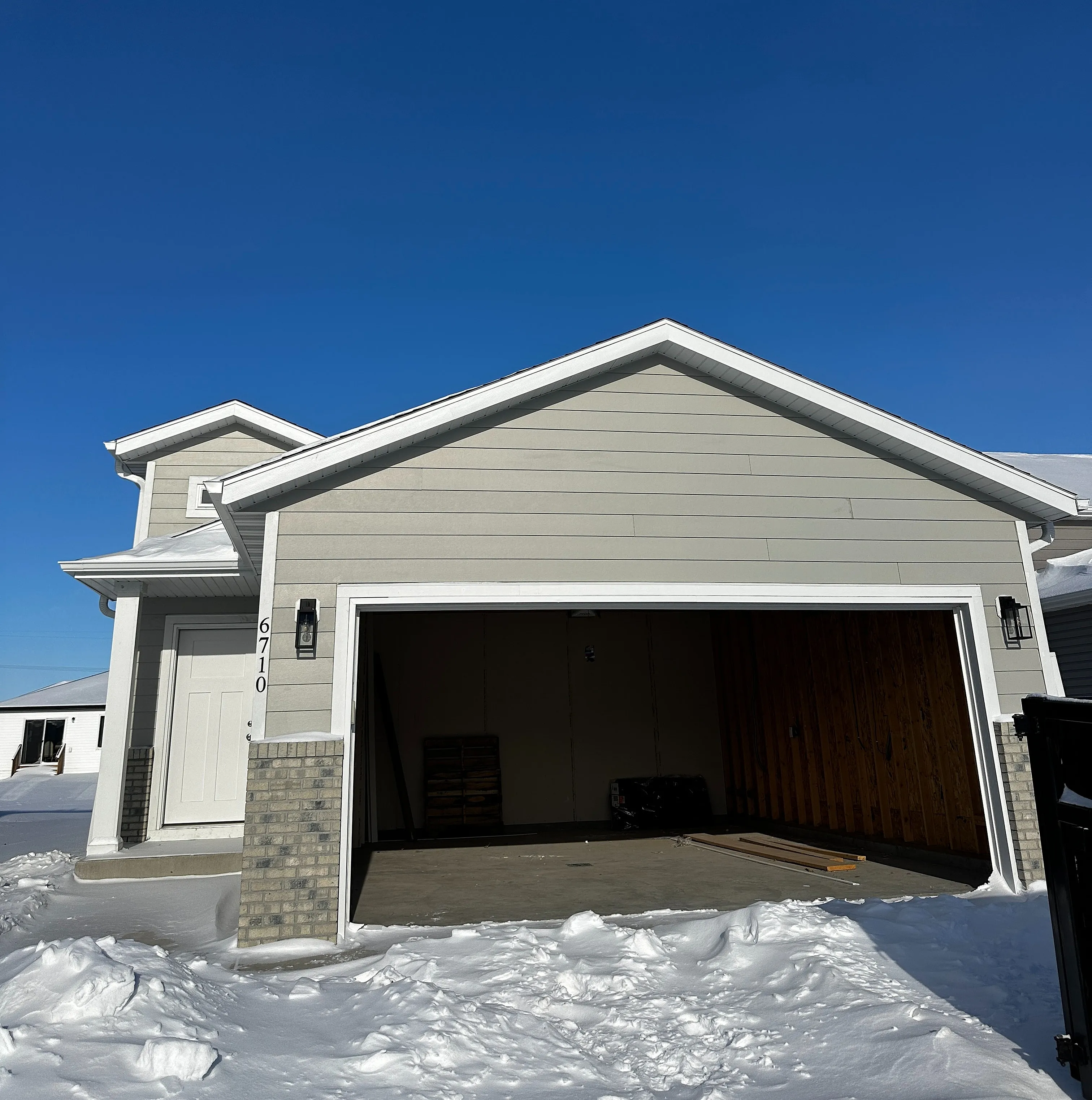 Charming single-story home with a spacious garage, set against a crisp blue sky and surrounded by fresh winter snow.