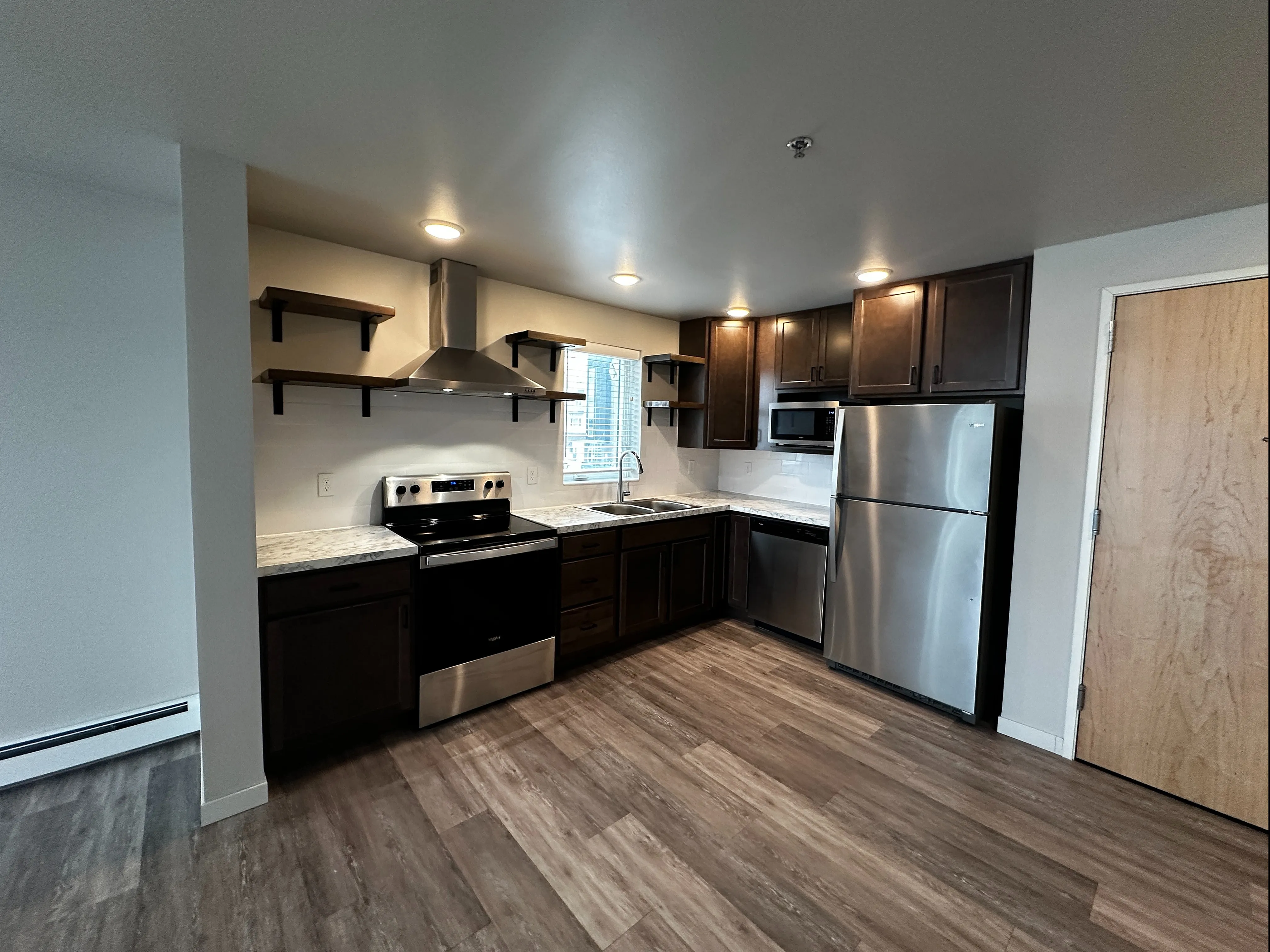 Modern kitchen with sleek dark wood cabinets, stainless steel appliances, and stylish open shelving.