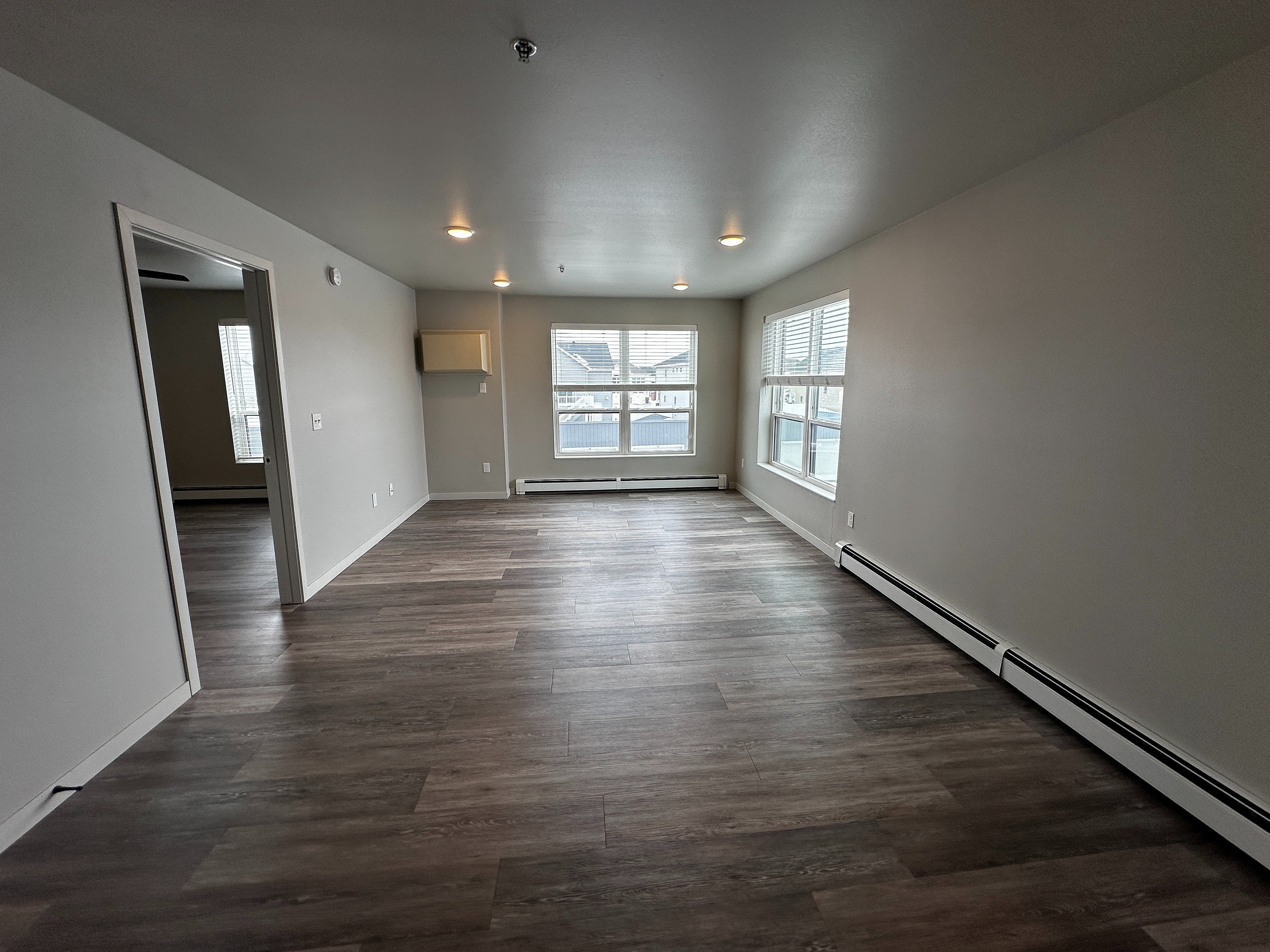 Bright and spacious living area with modern wood flooring, large windows, and sleek design in a contemporary apartment.